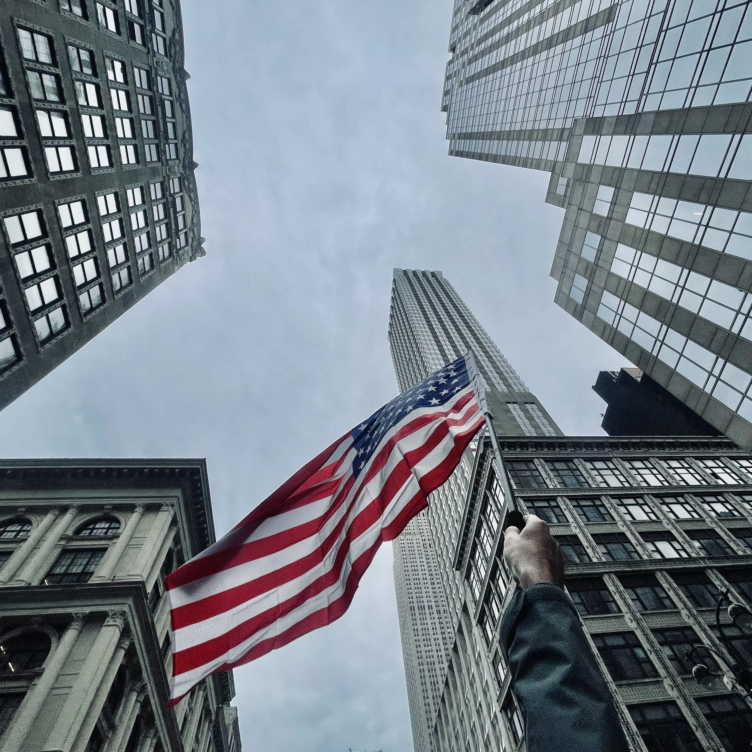 Looking up at tall skyscrapers with an American flag being held in the foreground.