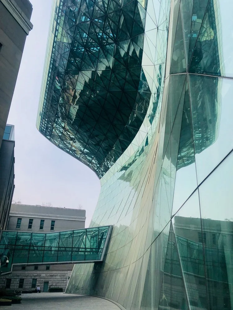 Modern glass skyscraper with reflective surfaces and a geometric design, connected to other buildings via glass bridges.