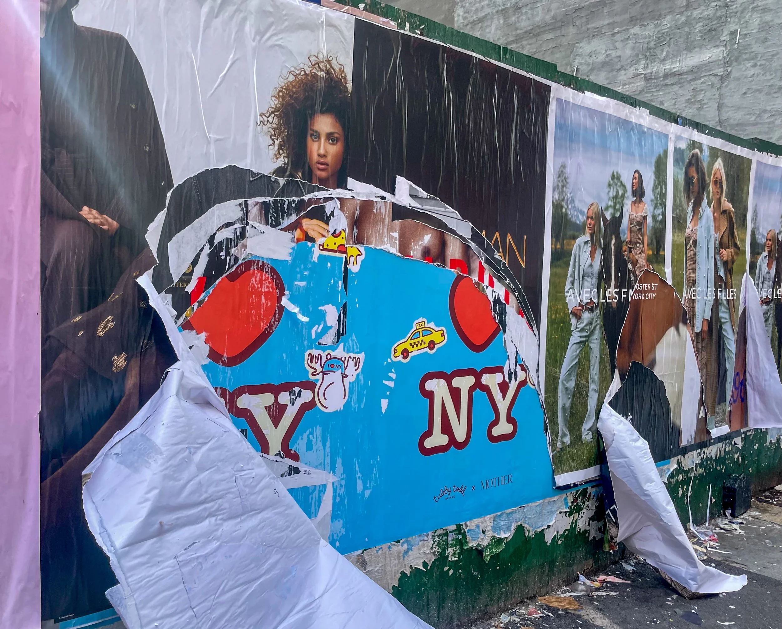 A torn outdoor poster display shows a woman with curly hair and light skin, alongside adjacent fashion photos of women walking outdoors wearing stylish outfits. The display includes a partly peeled New York City poster with a cartoon burger, a taxi, 