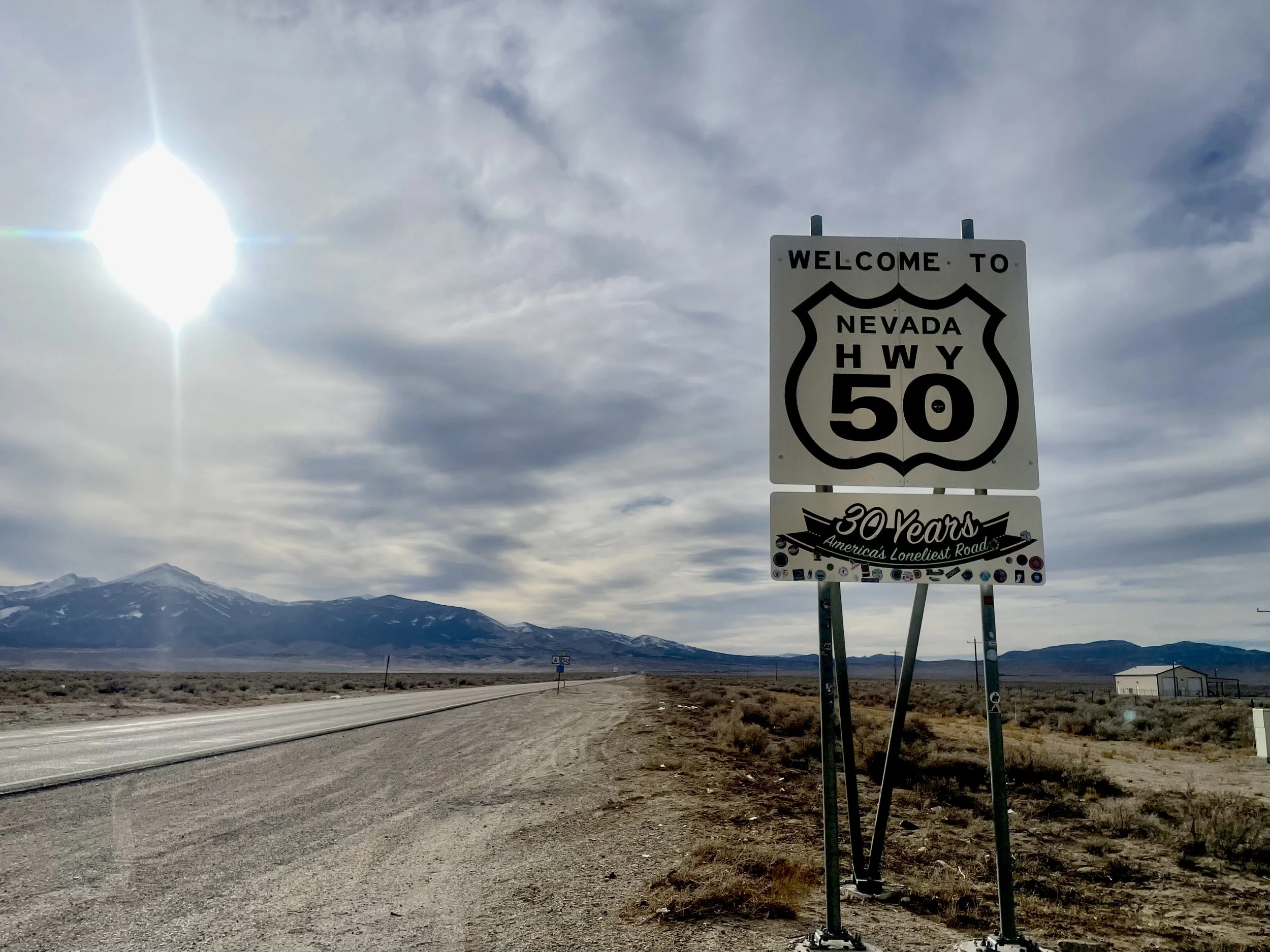 A road sign welcoming travelers to Nevada Highway 50, with a mountain range in the background and a partly cloudy sky, celebrating 30 years of the road.