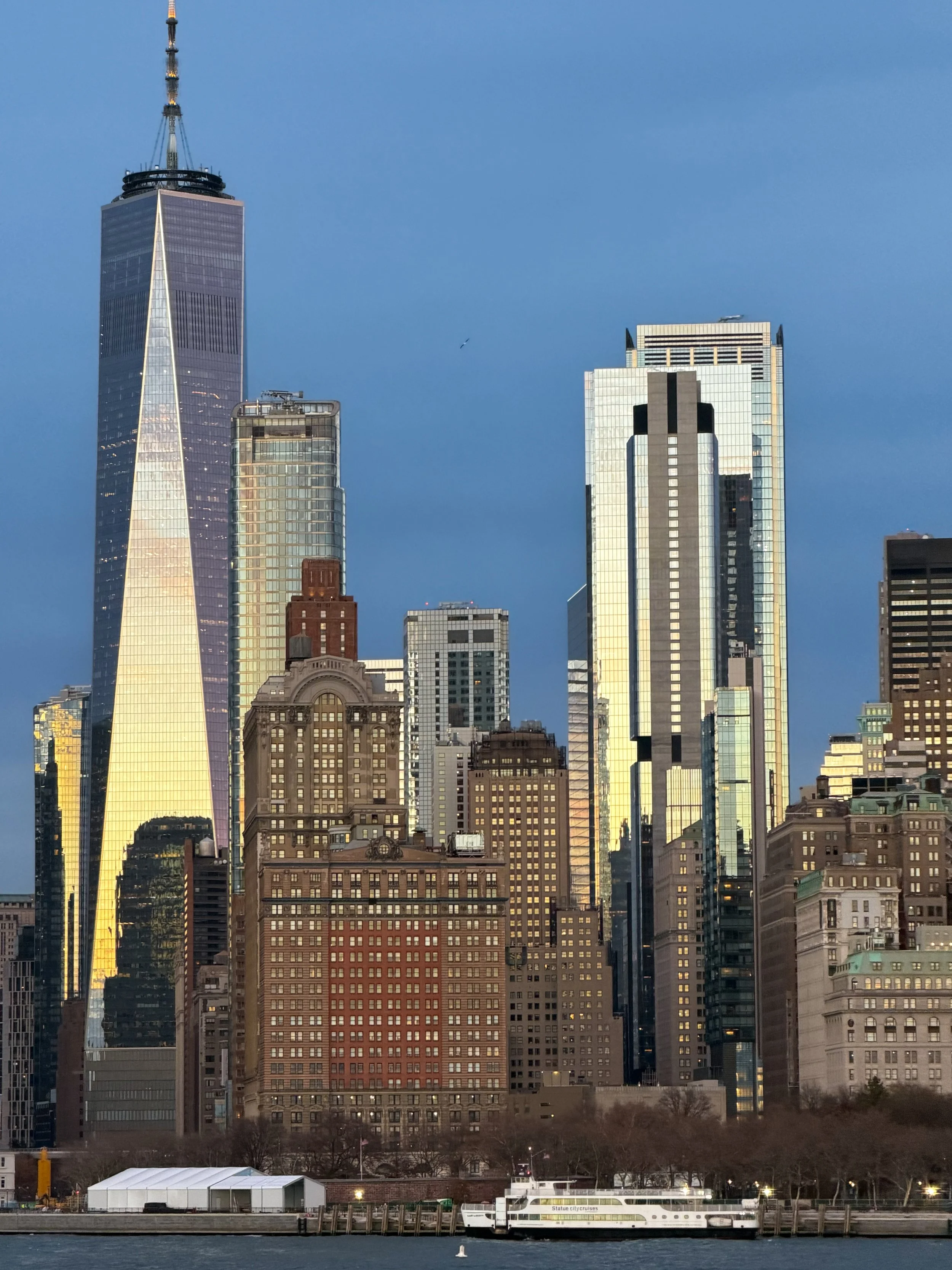 Sunset view of Manhattan skyline featuring One World Trade Center and modern skyscrapers.