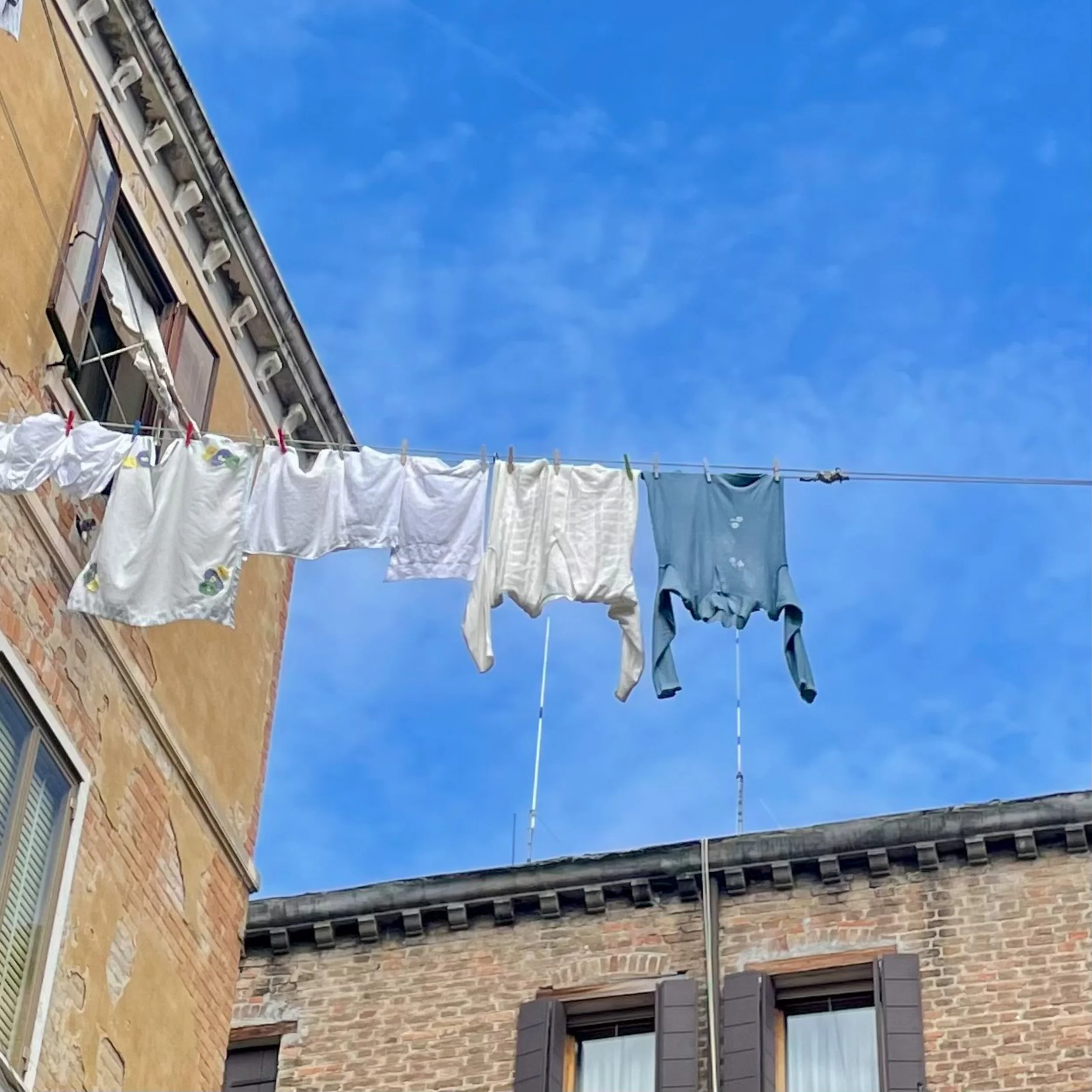 Clothes hanging on a clothesline outside between buildings under a blue sky.