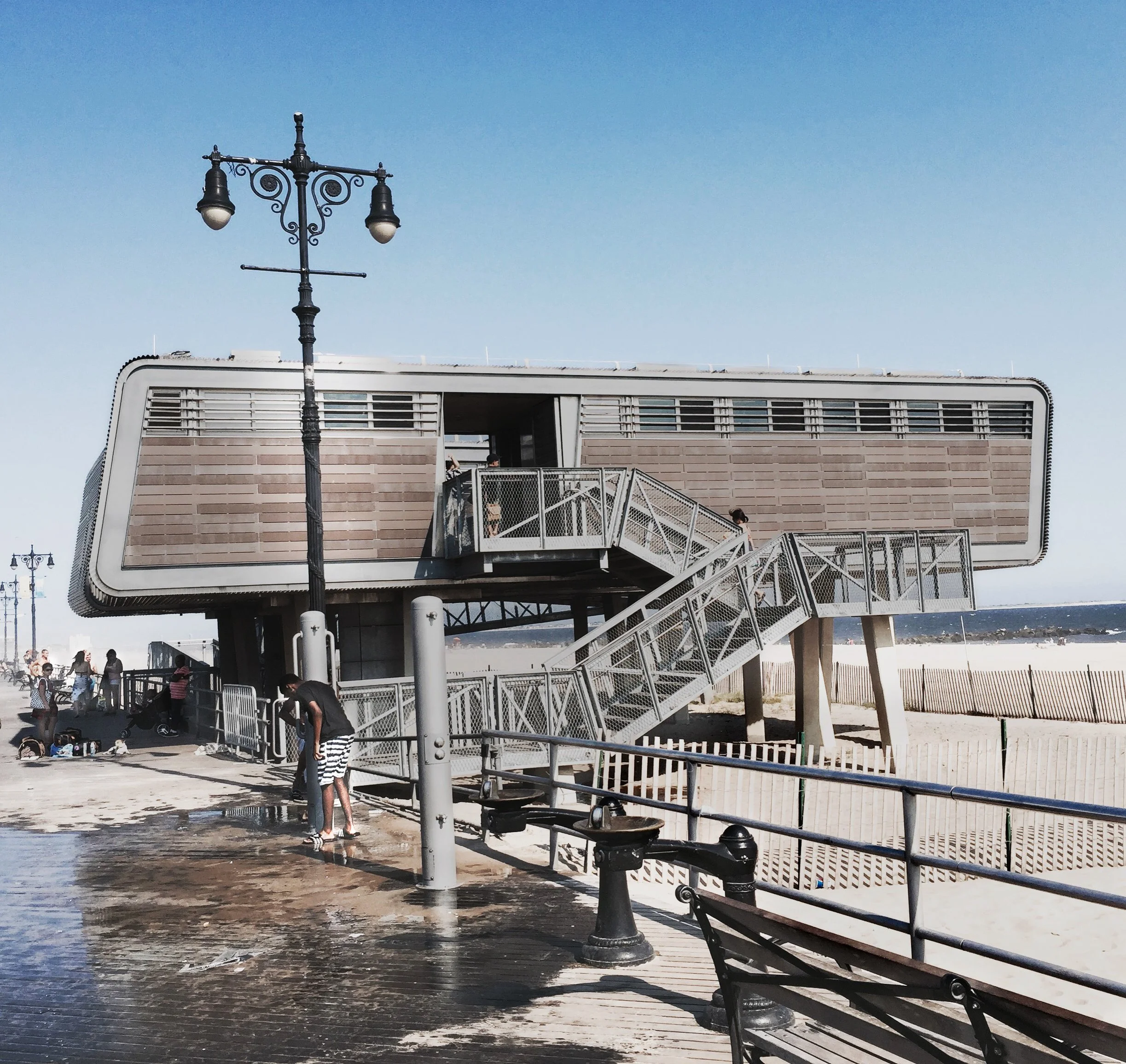 Beachside building with stairs and people near the water on a sunny day.