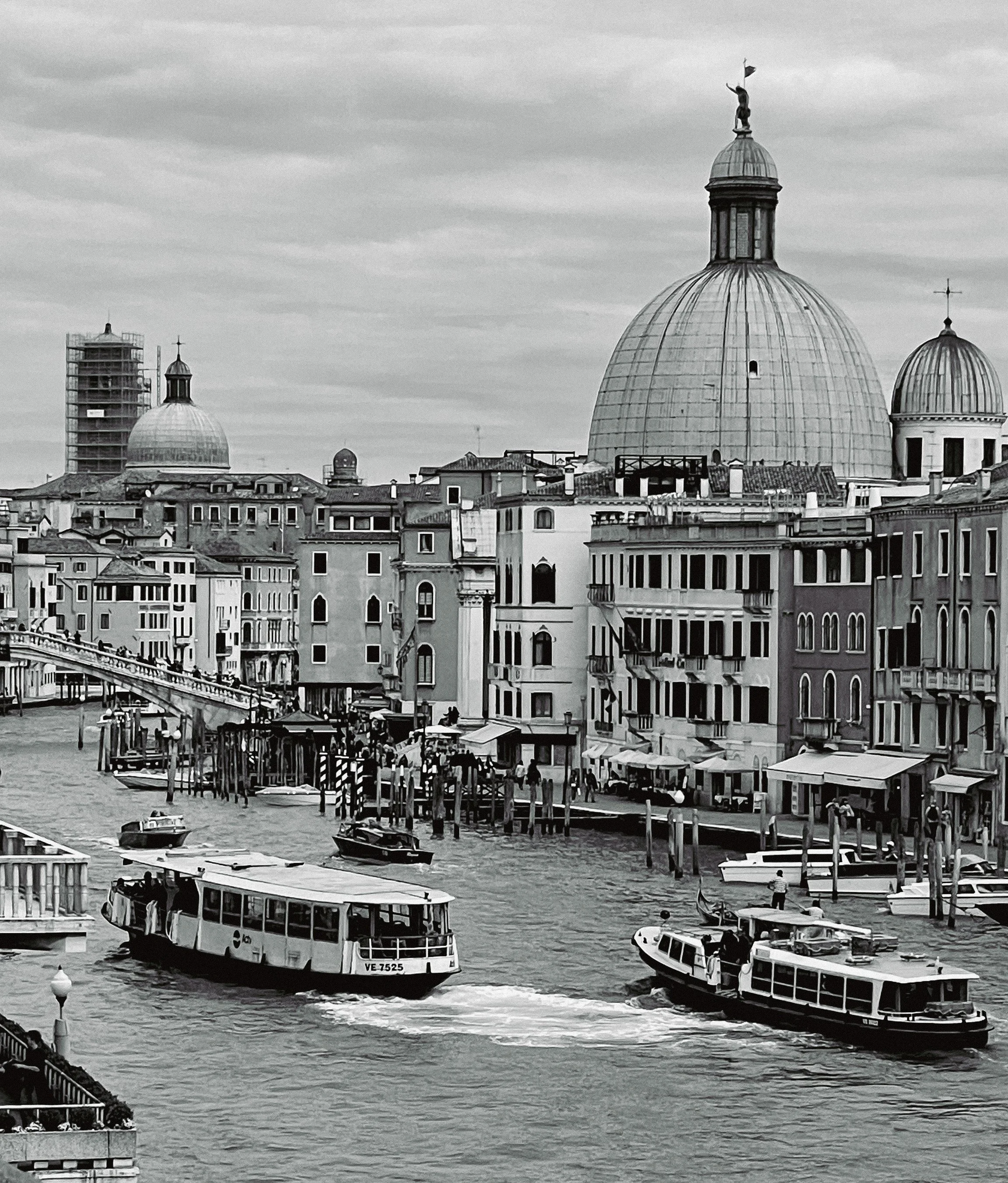 View of Venice canal with boats, historic buildings, and domed churches in black and white.