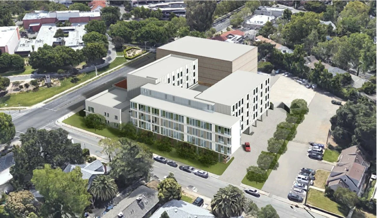 Aerial view of a modern multi-story office or apartment building with a parking lot, surrounded by trees and residential houses.