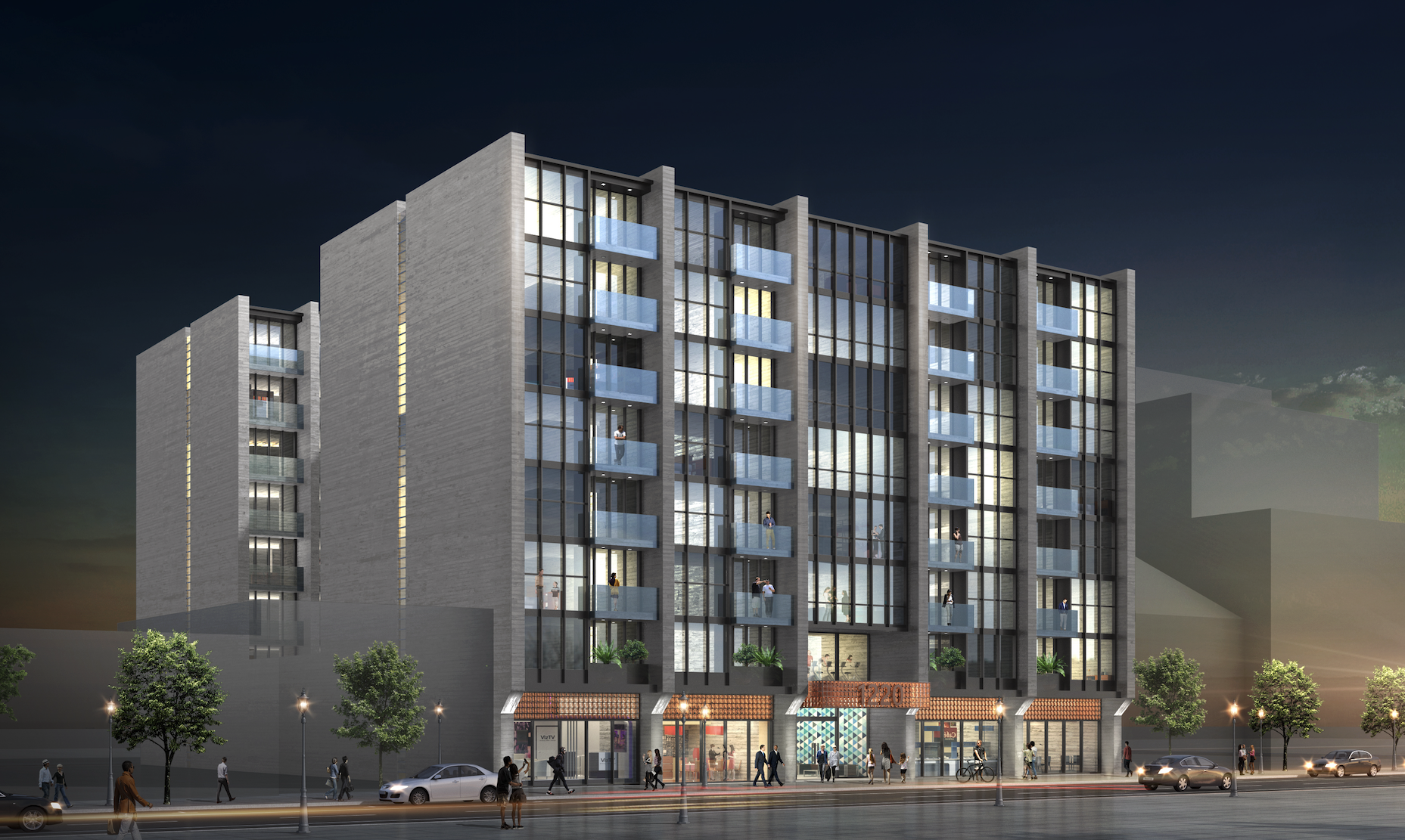 Nighttime view of a modern multi-story building with glass windows and balconies, people on the balconies and walking on the sidewalk below, trees in front, and cars parked or driving by on the street.