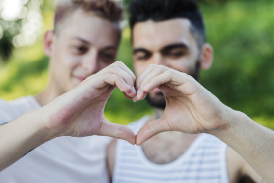 Two people forming a heart shape with their hands outdoors.