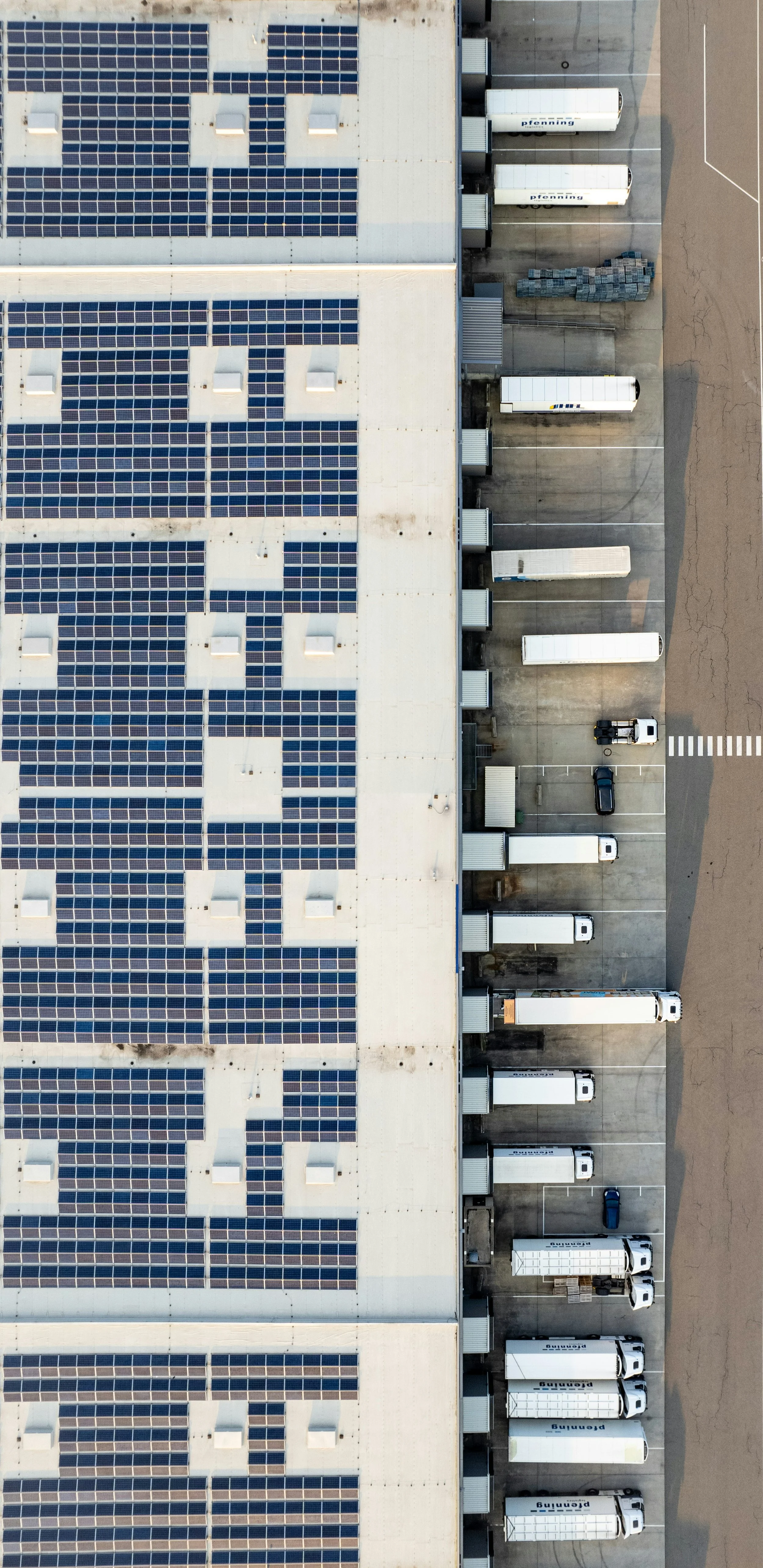 Aerial view of a warehouse with solar panels on the roof and trucks parked at loading docks.