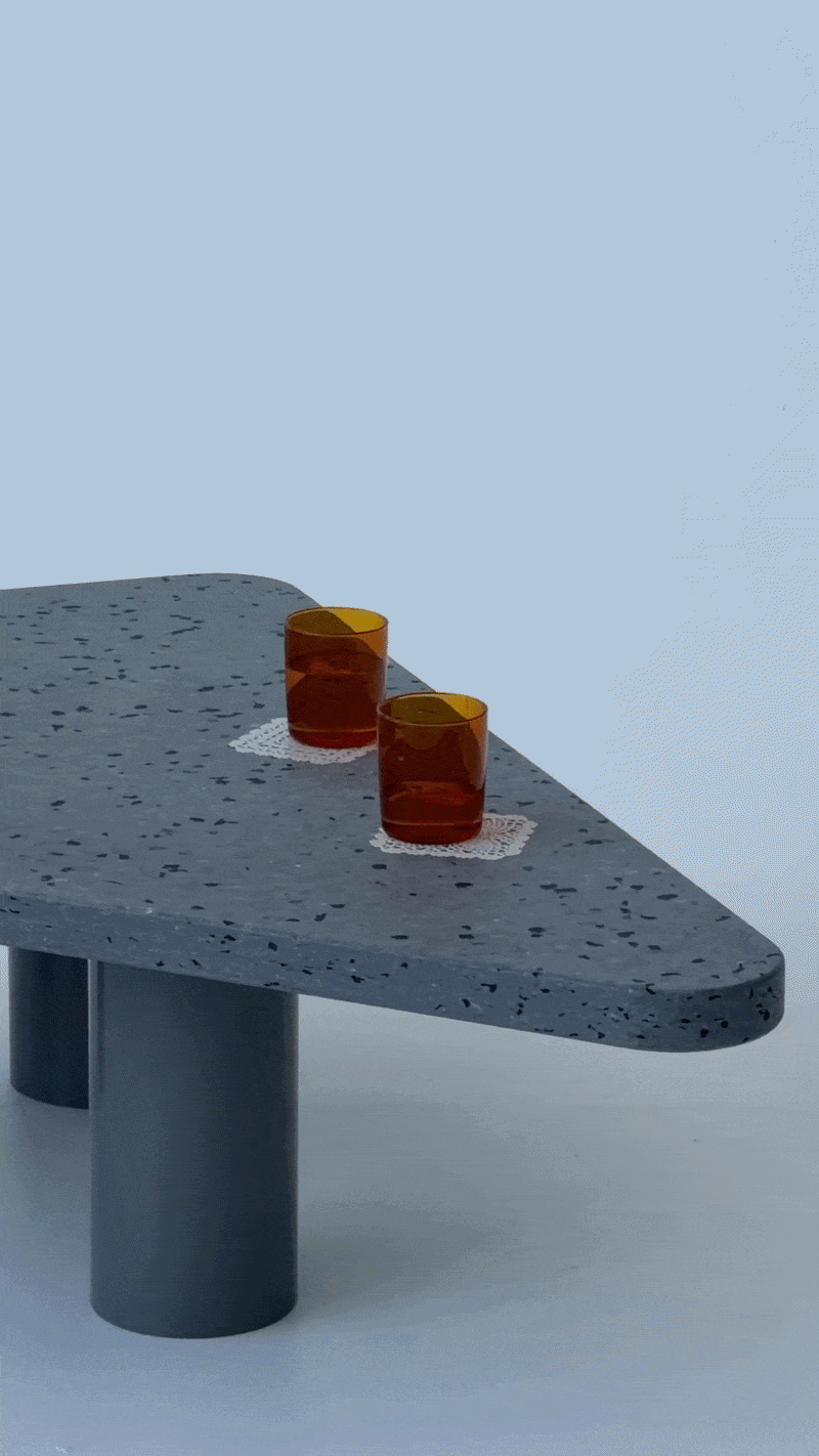 Two amber-colored glasses filled with dark liquid placed on small white doilies on a curved gray terrazzo table.
