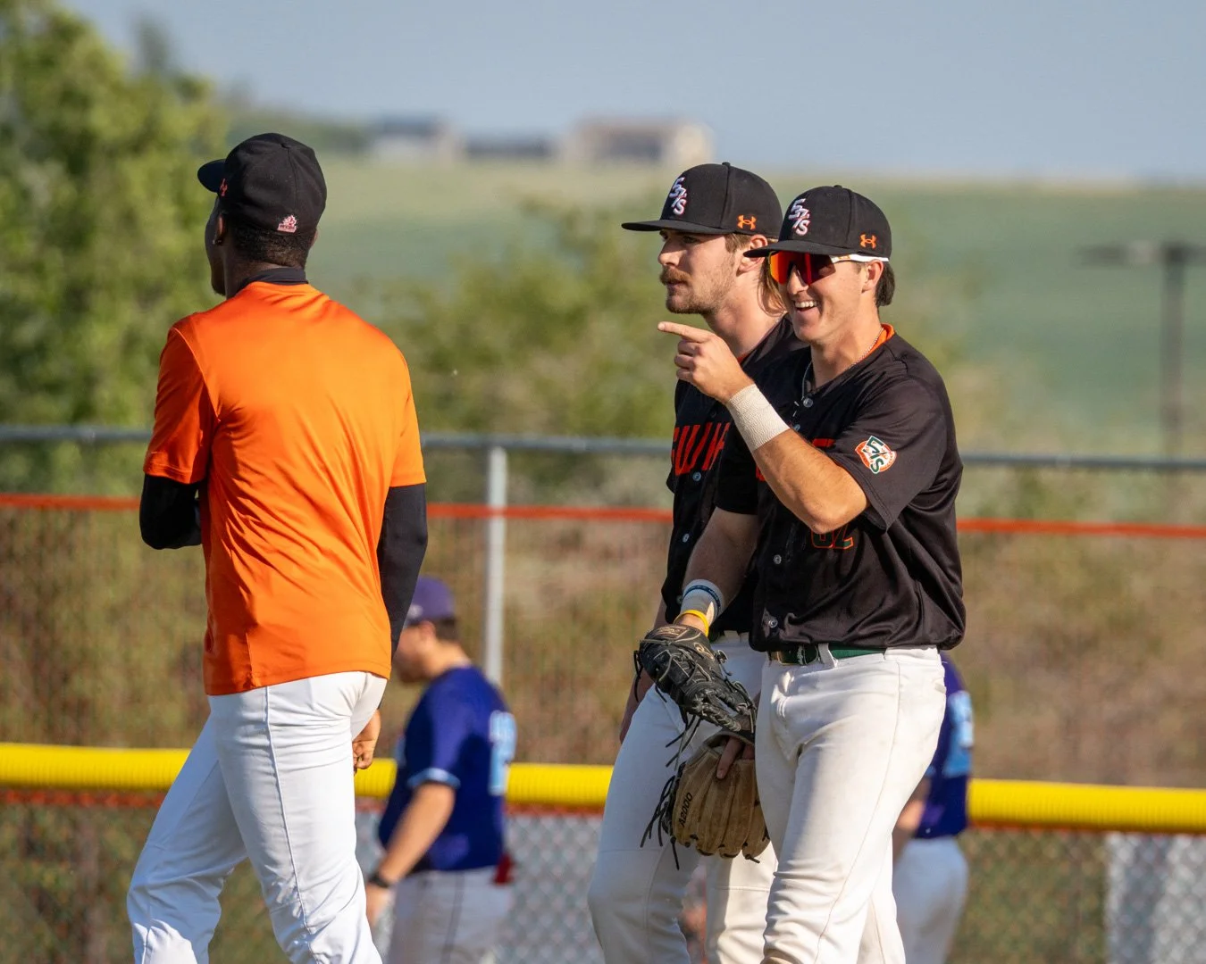 Three baseball players on a field, two of them are smiling and talking, one is facing away from the camera.