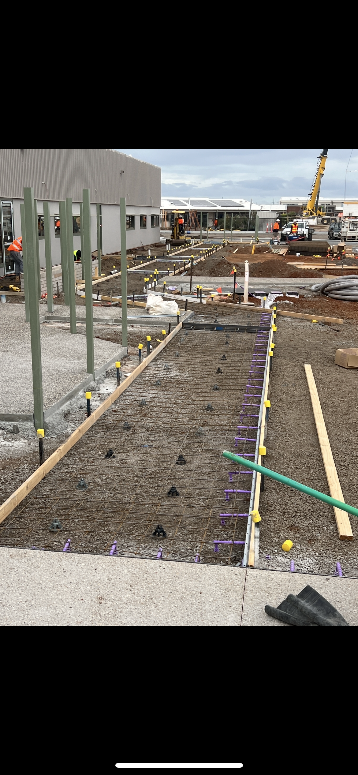 Construction site with workers building a sidewalk or pathway with concrete and rebar, with equipment and materials around.