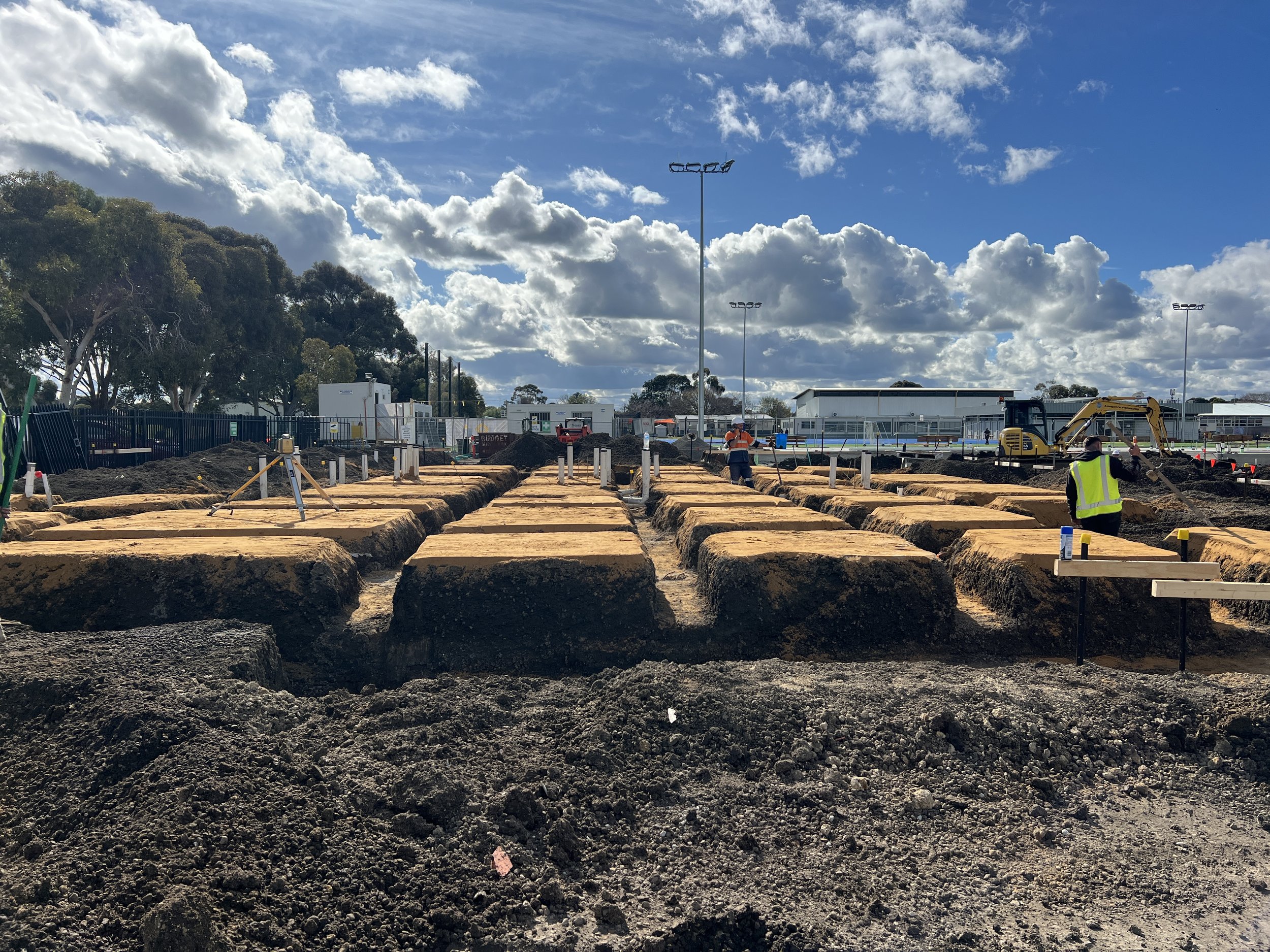 Construction site with workers, machinery, dirt trenches, and a partly cloudy sky.