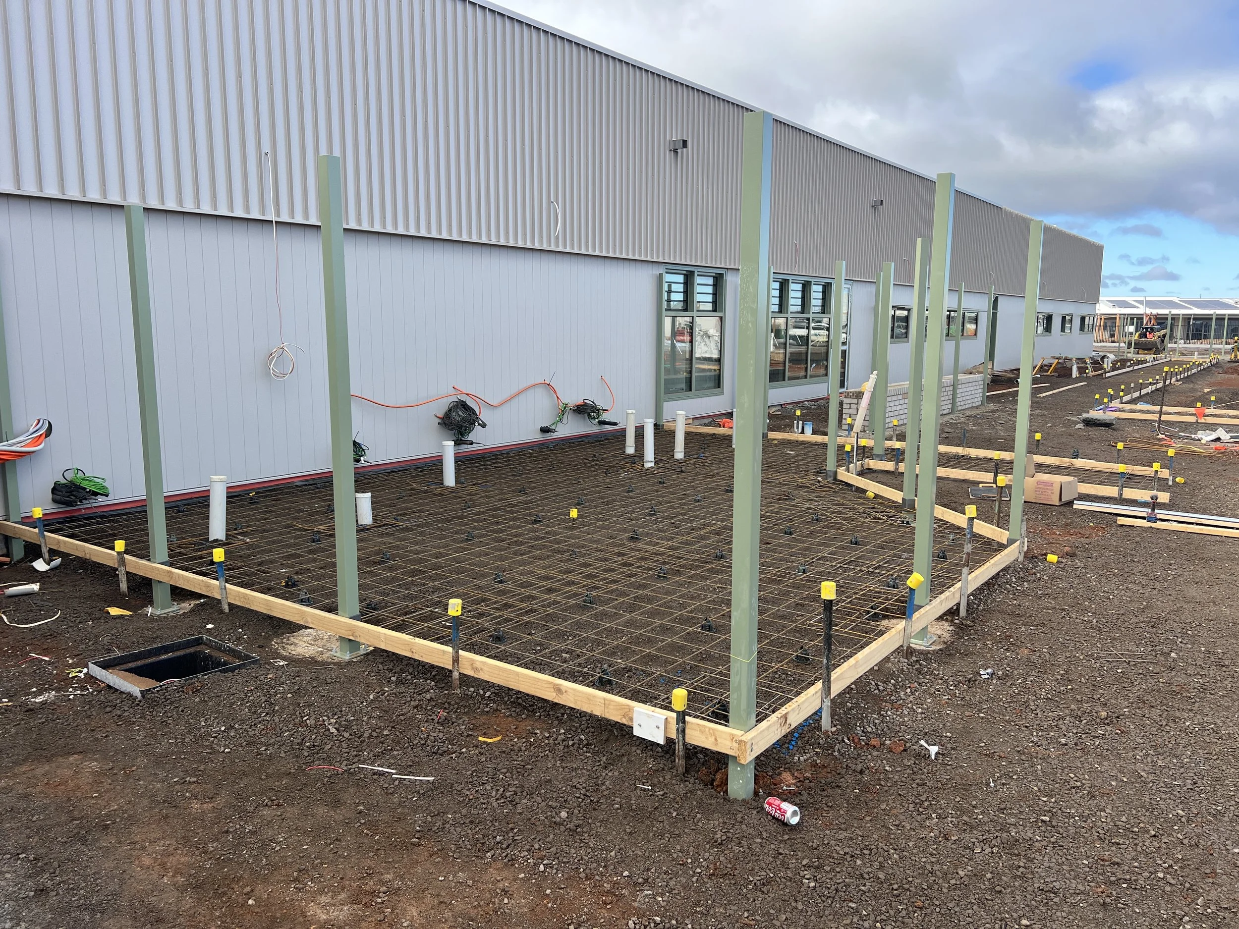 Construction site with a concrete slab foundation framed with wooden and metal supports, electric wiring, and building walls in the background.