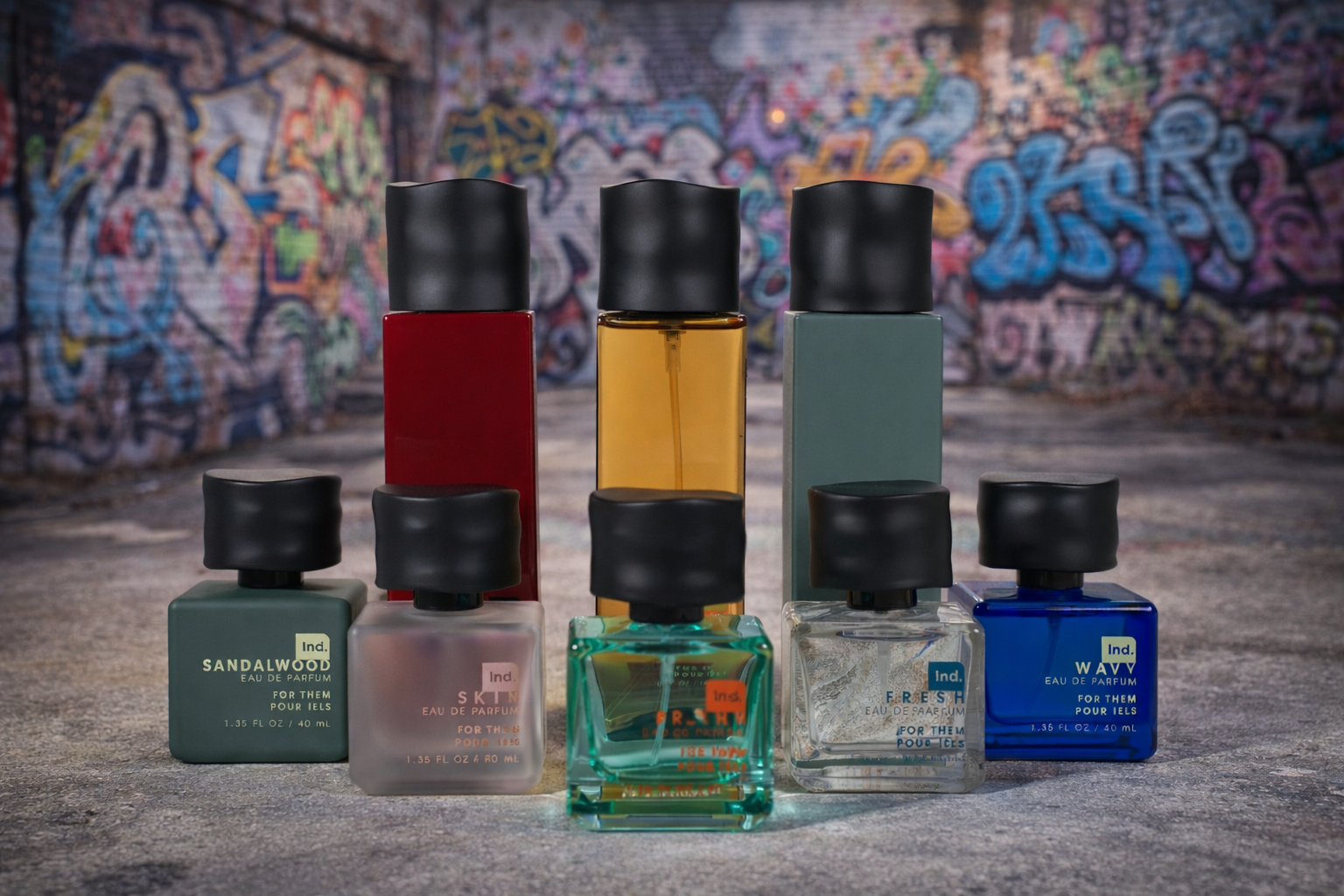 Five bottles of perfume arranged in front of a colorful graffiti wall, with three taller bottles at the back and two smaller bottles in the front, each with black caps and varied colors.
