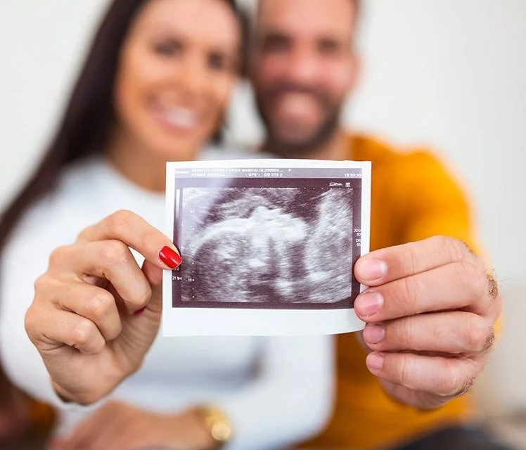 A smiling couple holding an ultrasound picture of a fetus.