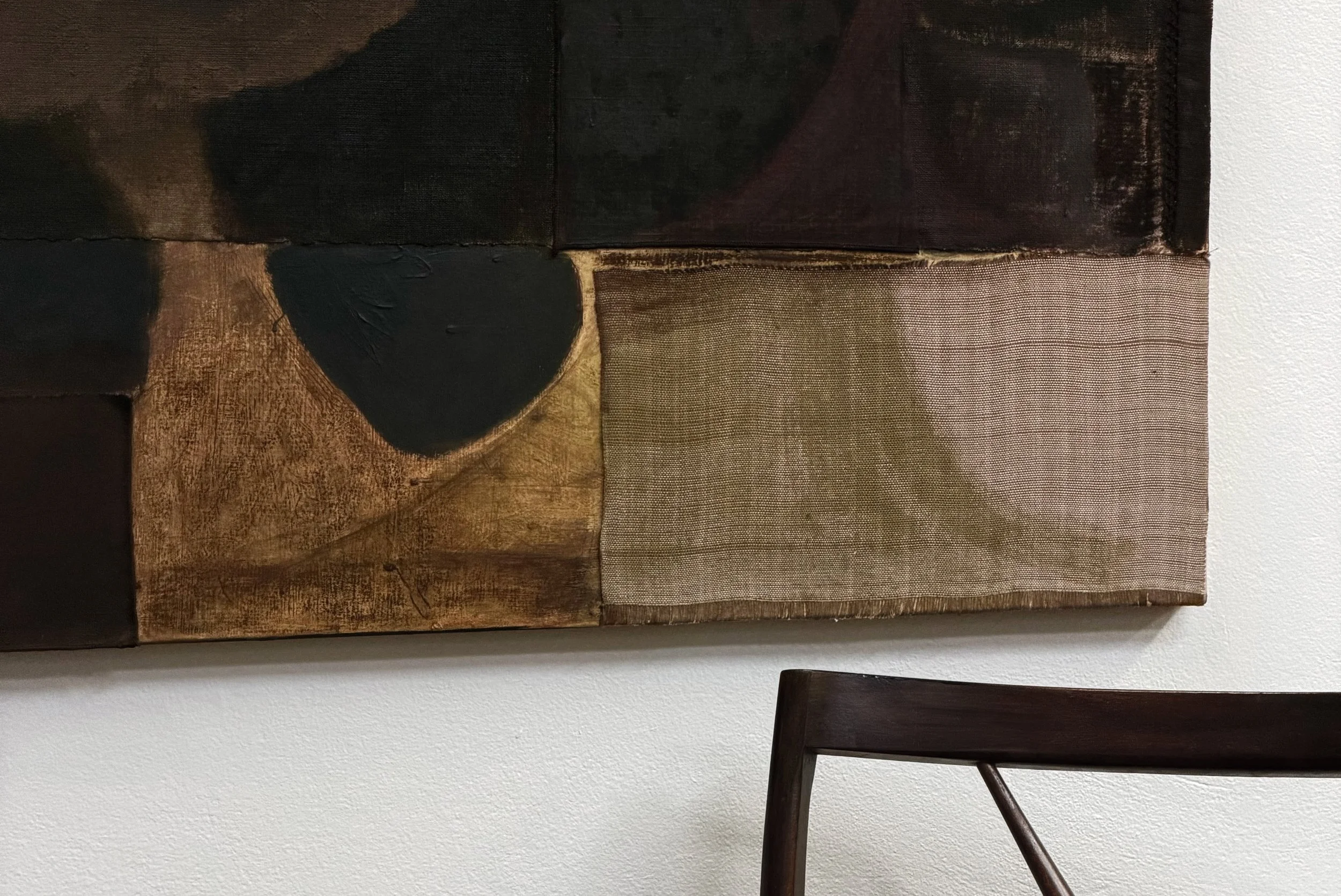 Close-up of a textured mixed-media art piece with acrylic paint, textiles, and fabric sections, mounted on a white wall