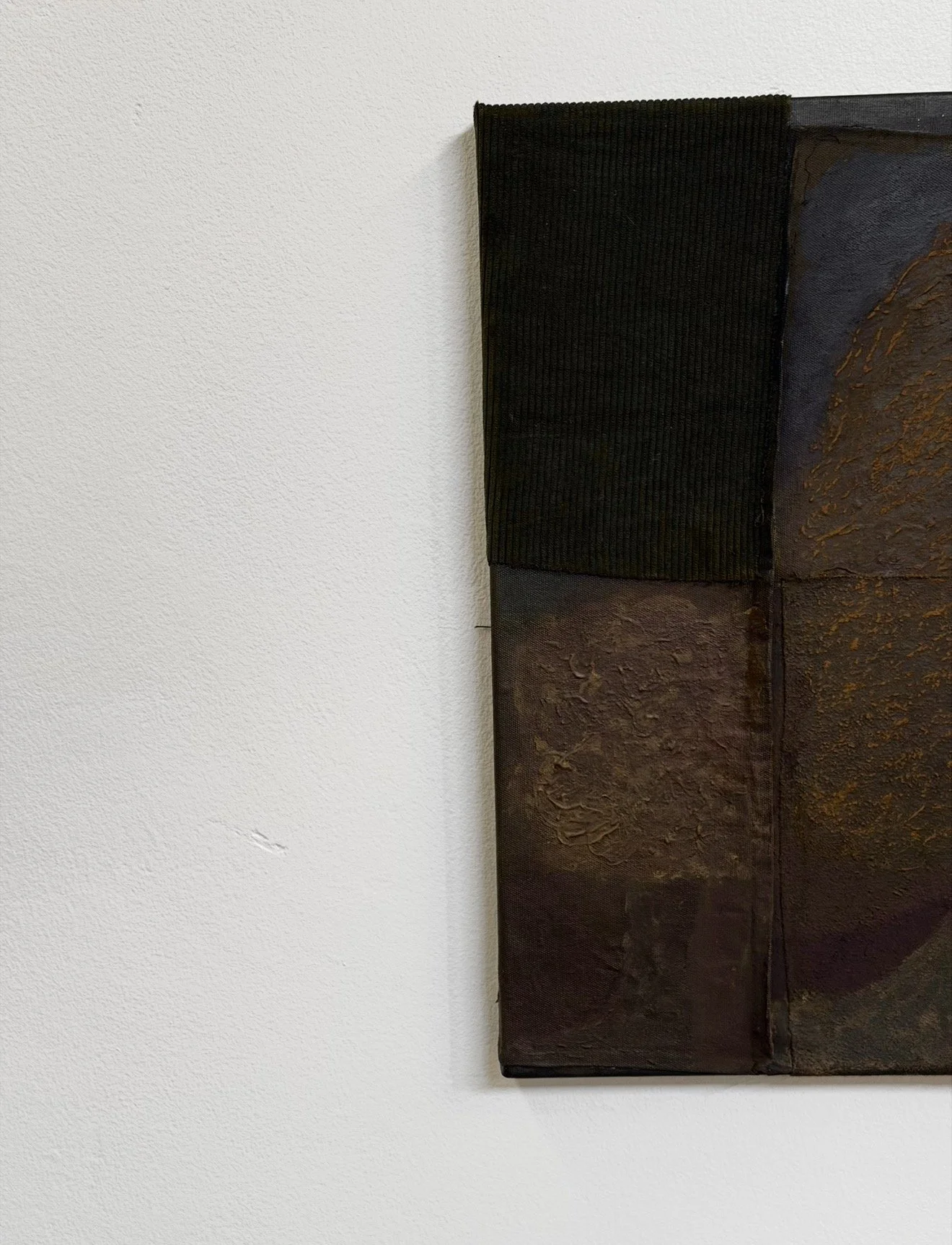 Close-up of a textured, brownish-red painting with earthy tones, partially covered by a black fabric border, hanging on a white textured wall.