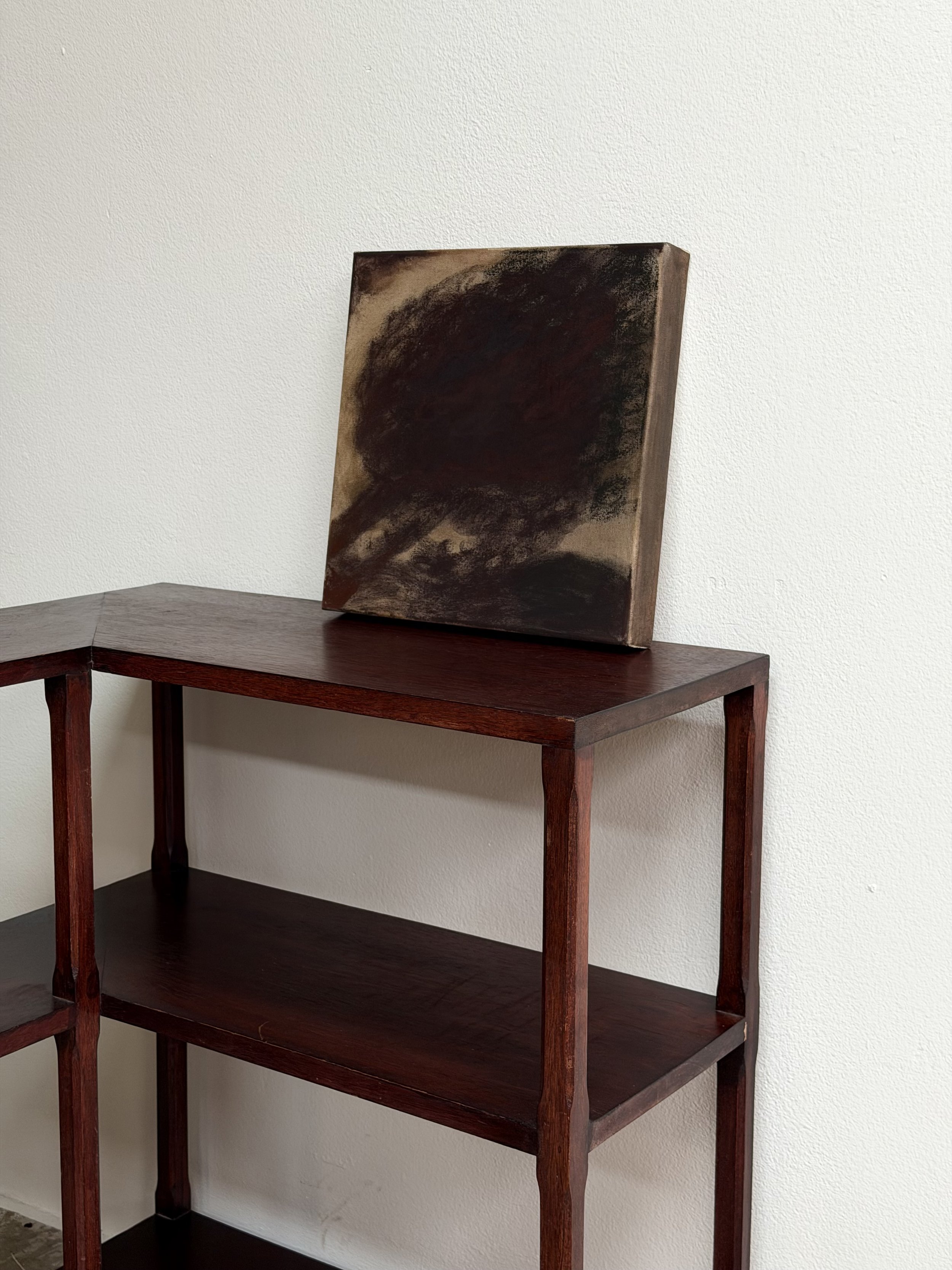 A framed abstract painting resting on a wooden shelf against a white textured wall.