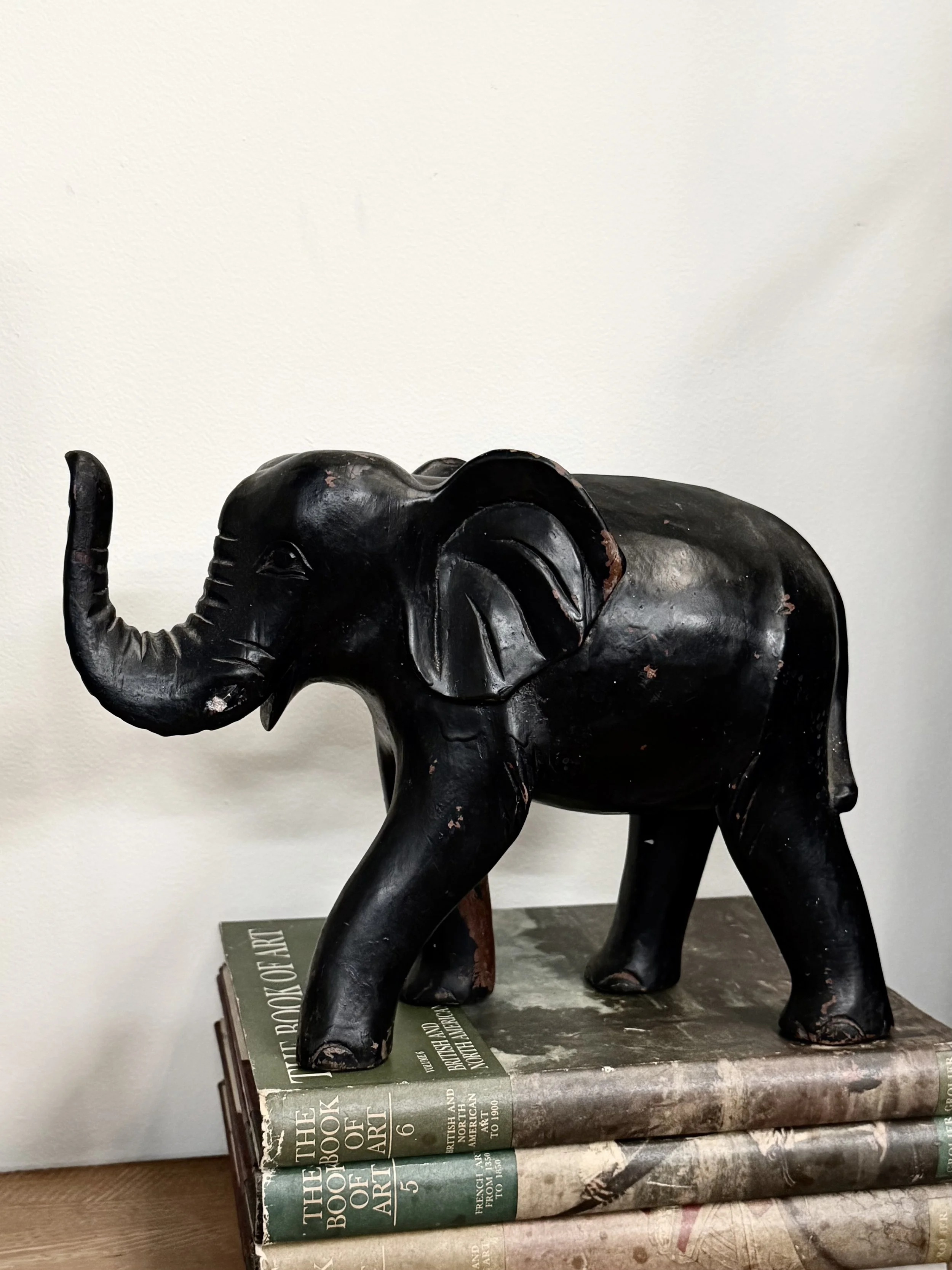 A black wooden elephant sculpture placed on top of a stack of books.