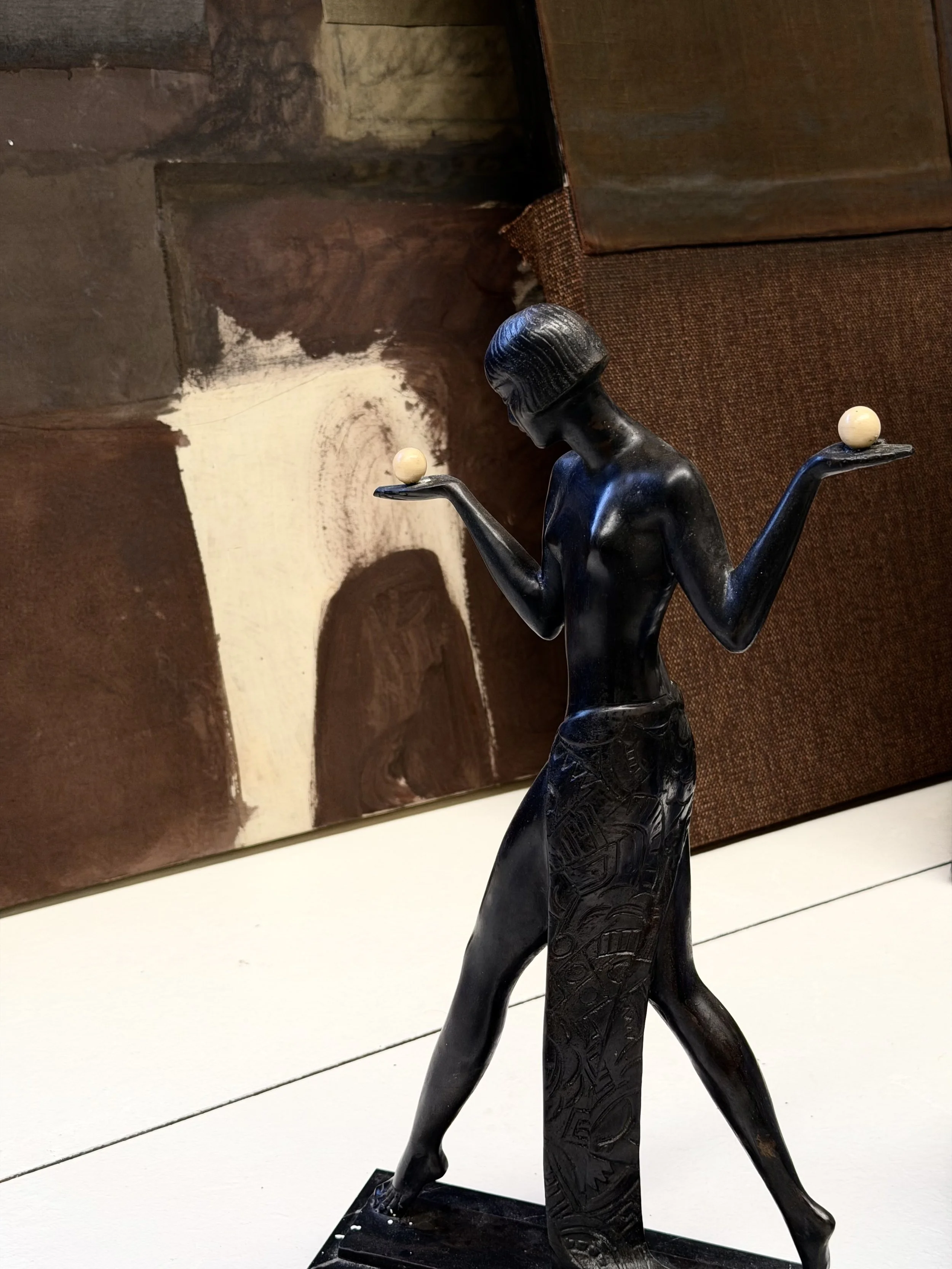A black sculpture of a woman walking with two small orbs balanced on her hands.