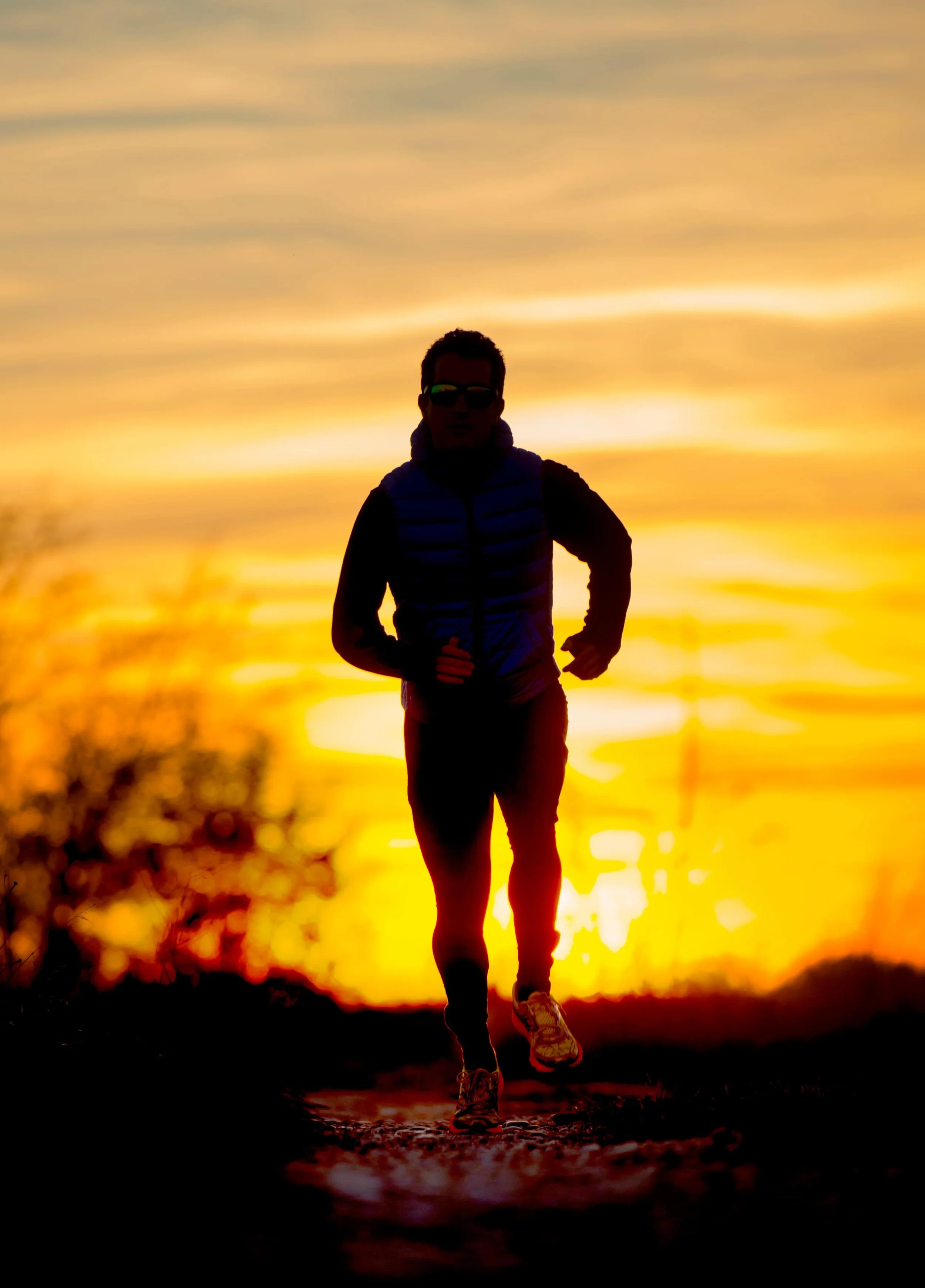 An endurance athlete running along the road with the sunrise in the background.