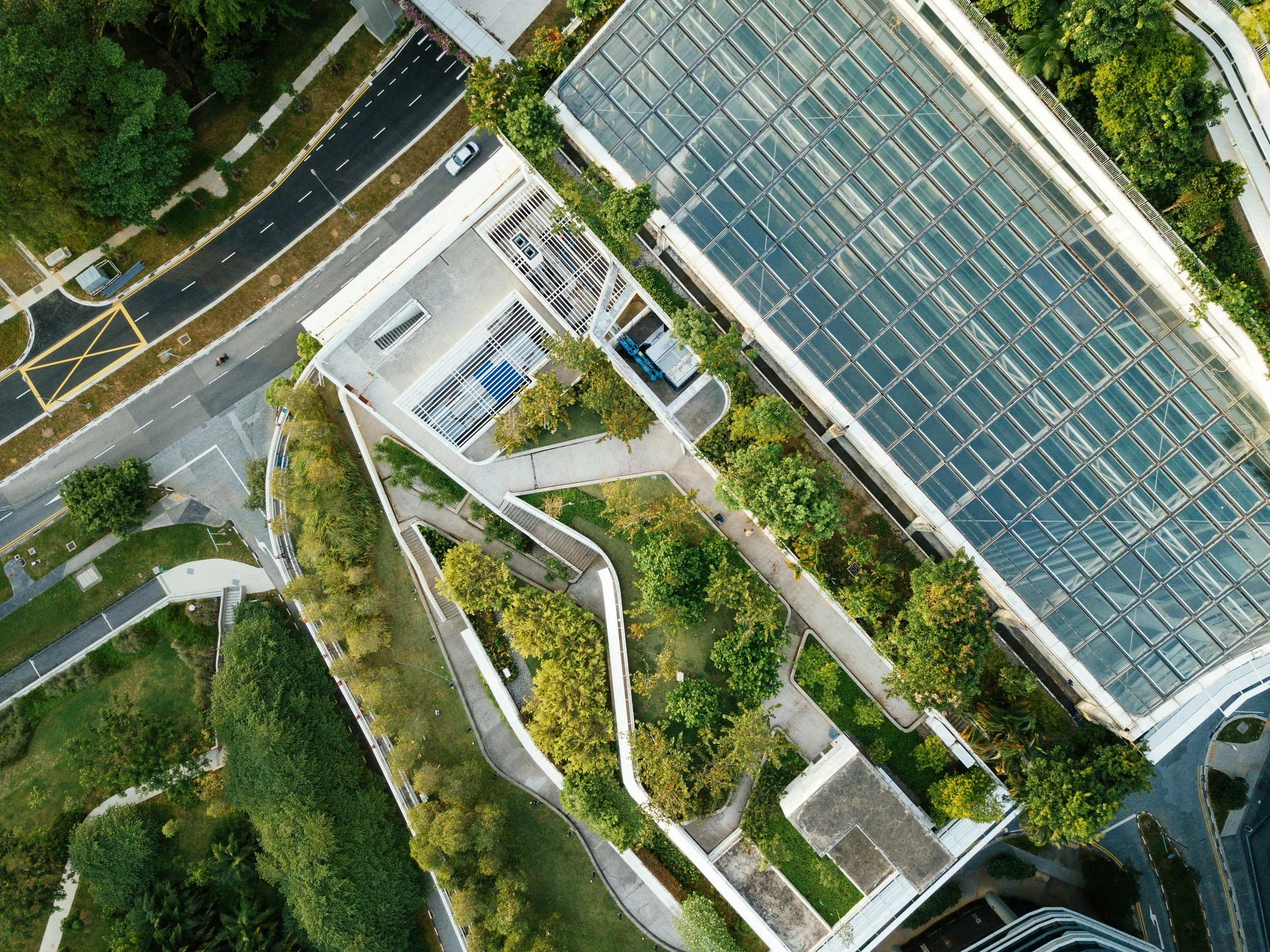 An aerial view of a modern urban area with green trees, landscaped walkways, and a building with a glass roof.