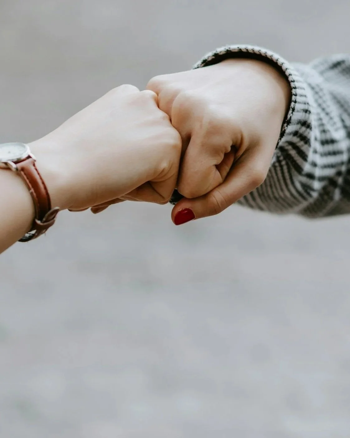 Two people performing a fist bump, one wearing a watch and the other with painted nails and a striped sleeve.