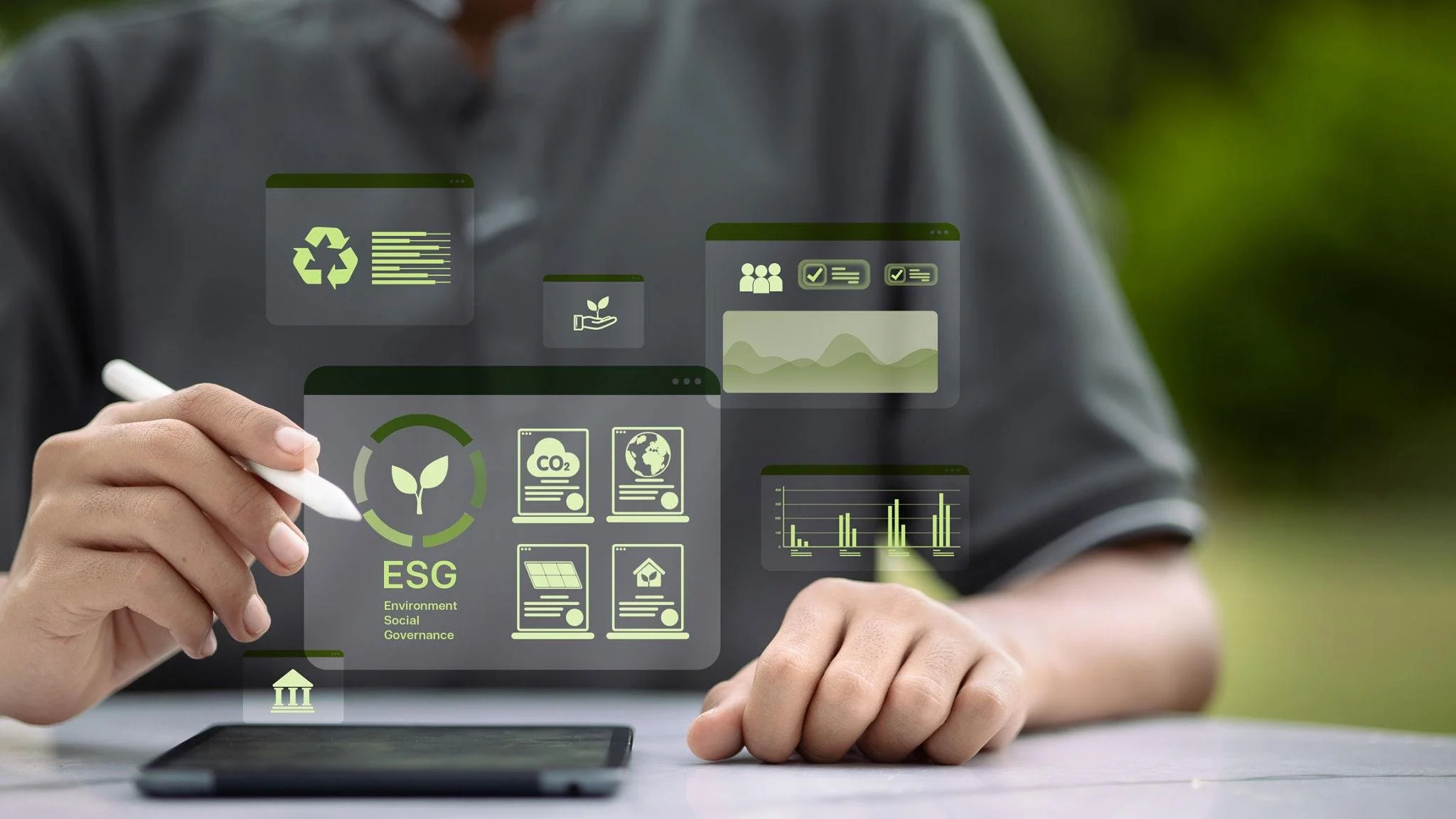 Person holding a stylus writing on a tablet with digital icons related to ESG, environment, social, and governance concepts, including charts, graphs, and sustainability symbols.