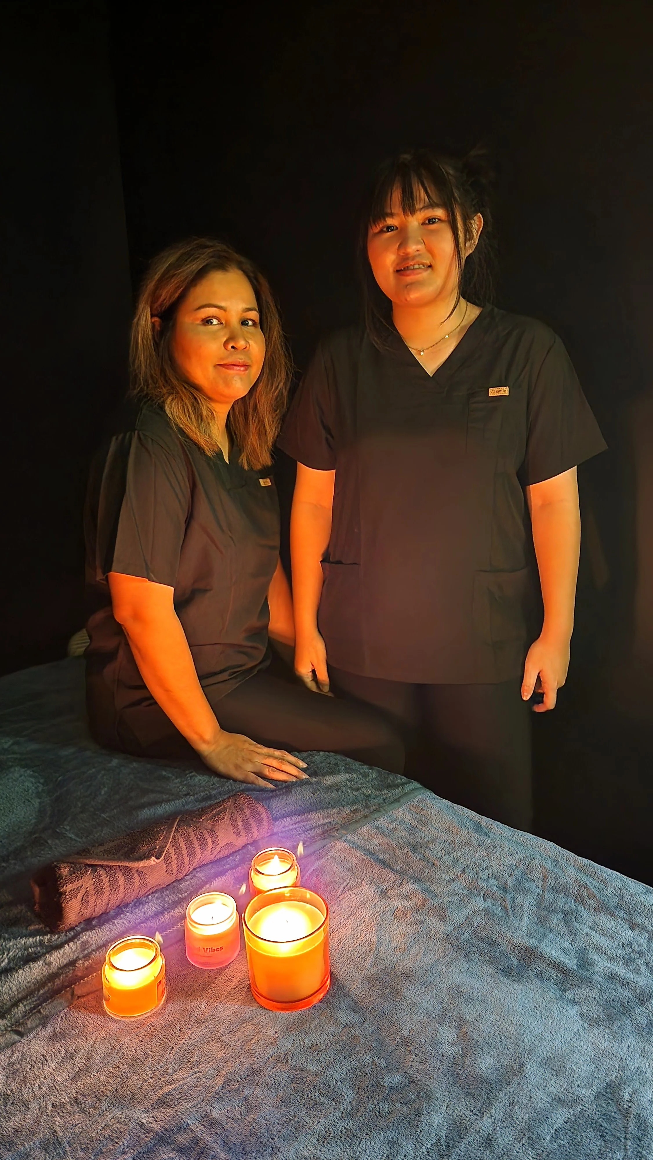 Patti and Pang, Thai massage therapists at Healing Touch Thai Massage, Sydenham Christchurch, beside a candlelit treatment table.