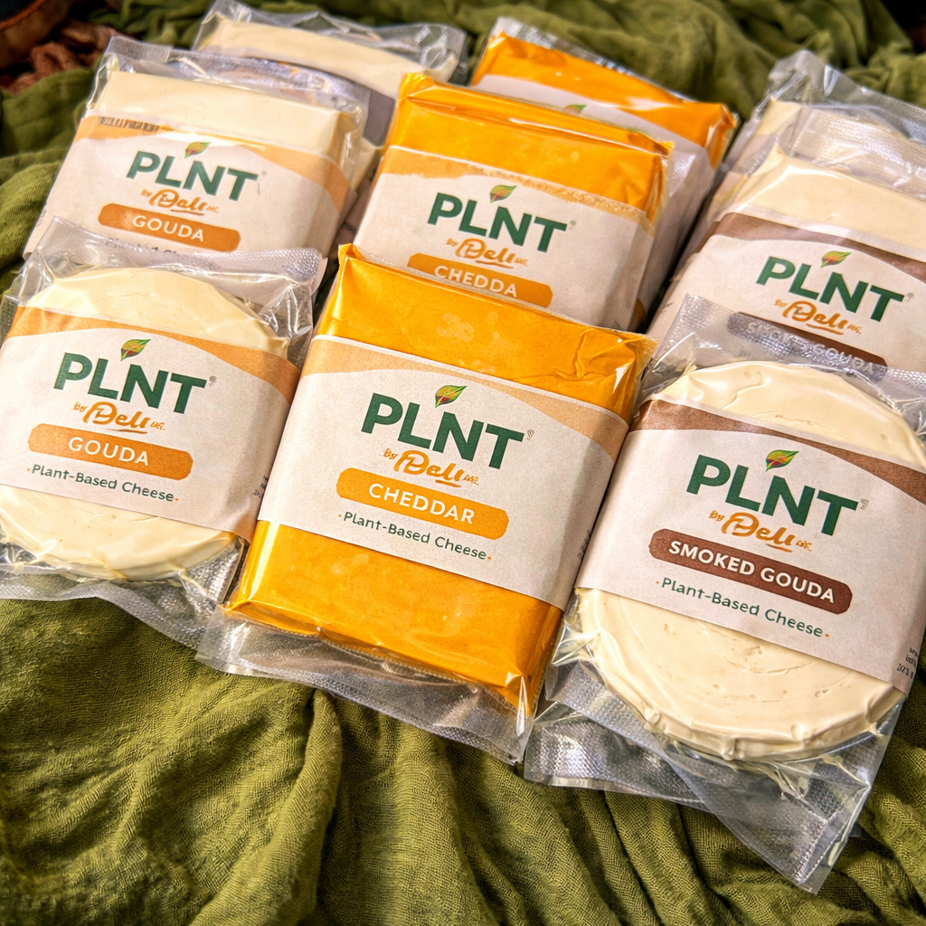 Various packages of plant-based cheese from the brand PLNT by Deli, including gouda, cheddar, and smoked gouda, displayed on a green fabric background.