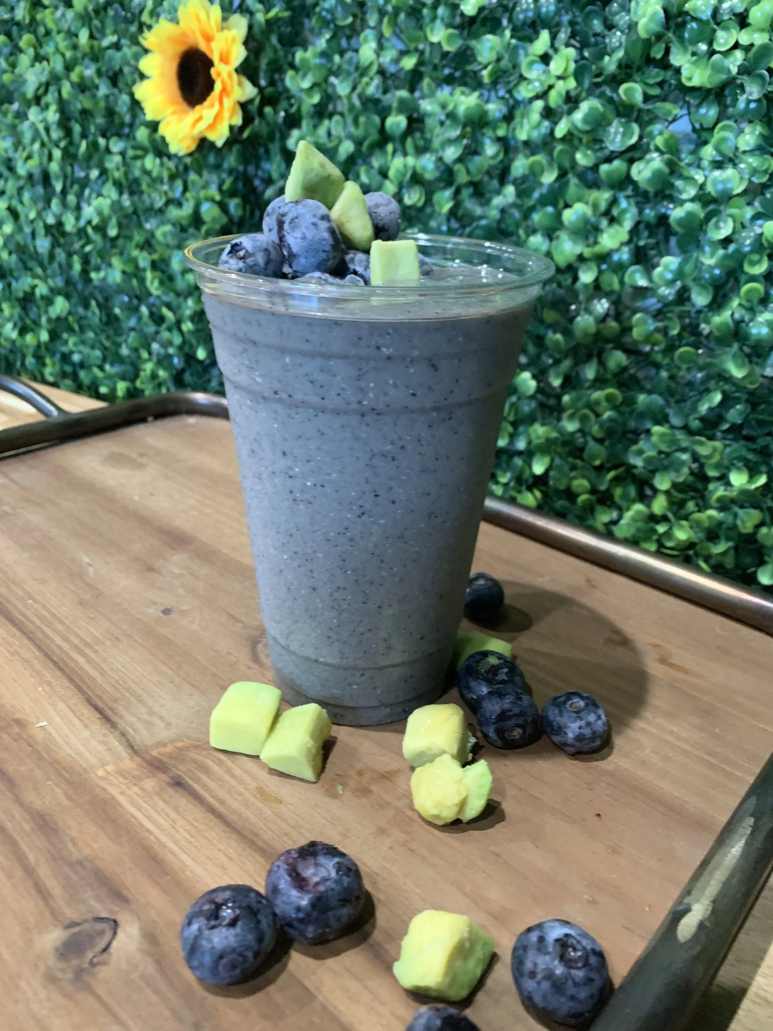 RHW’s Blueberry Avocado smoothie in a clear cup with blueberries and avocado pieces on a wooden tray.