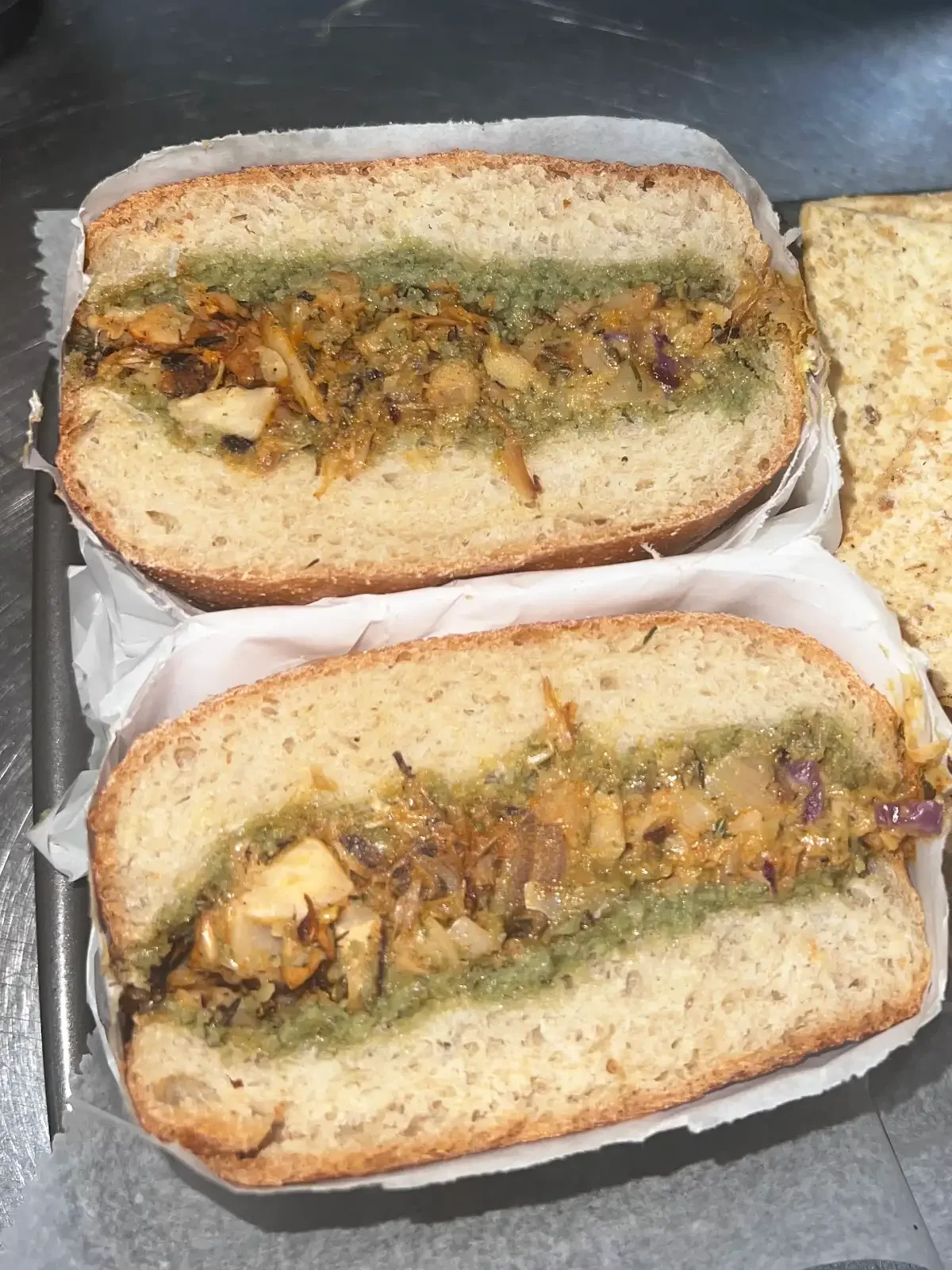 Two halves of RHW Chkn Pesto Panini with seasoned jackfruit, onions and basil pesto on toasted bread
