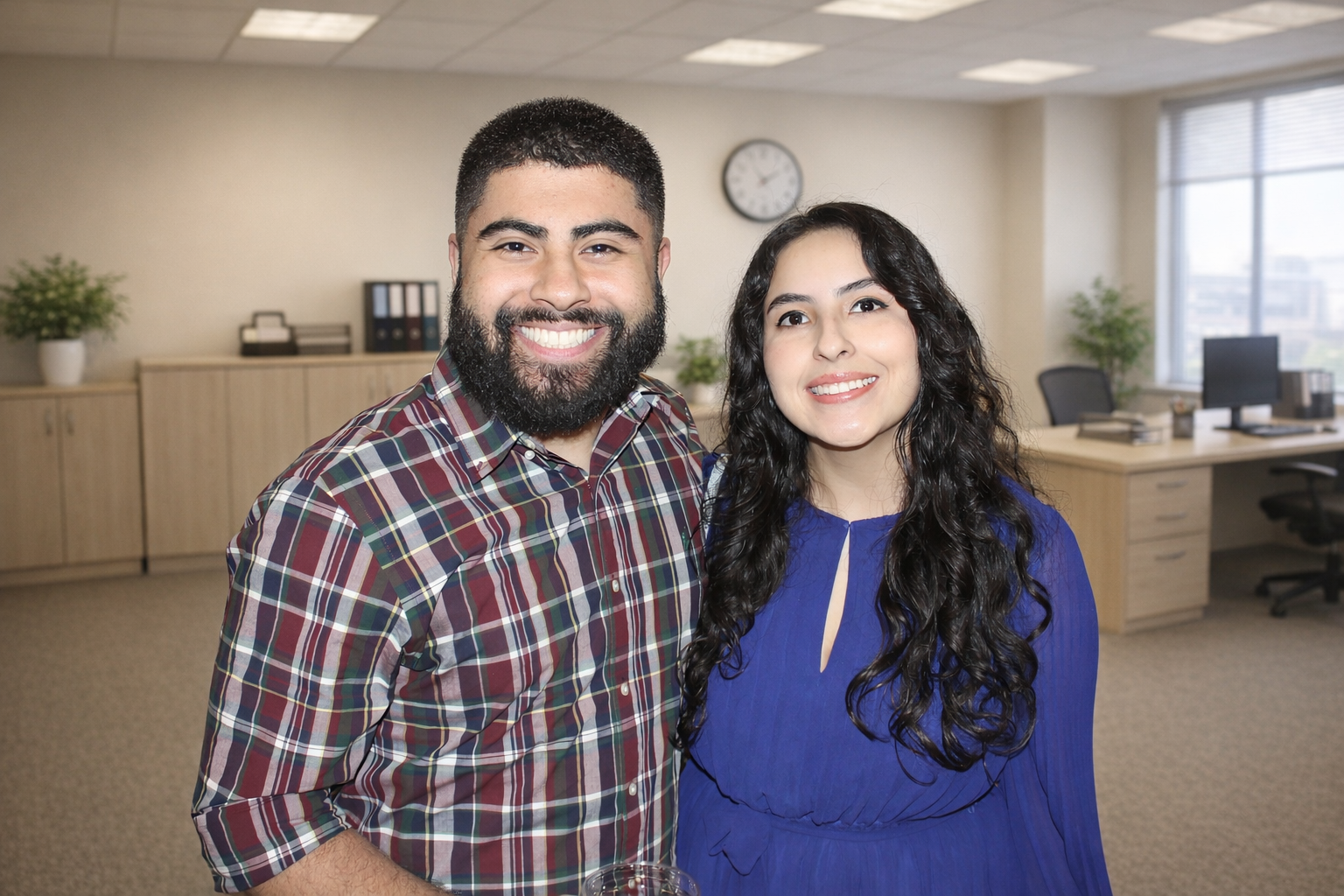 A smiling man with a beard and a woman with long curly hair posing together in an office setting.