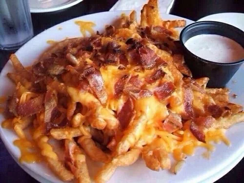 Plate of cheesy nachos topped with bacon bits, served with black and white dipping sauces.