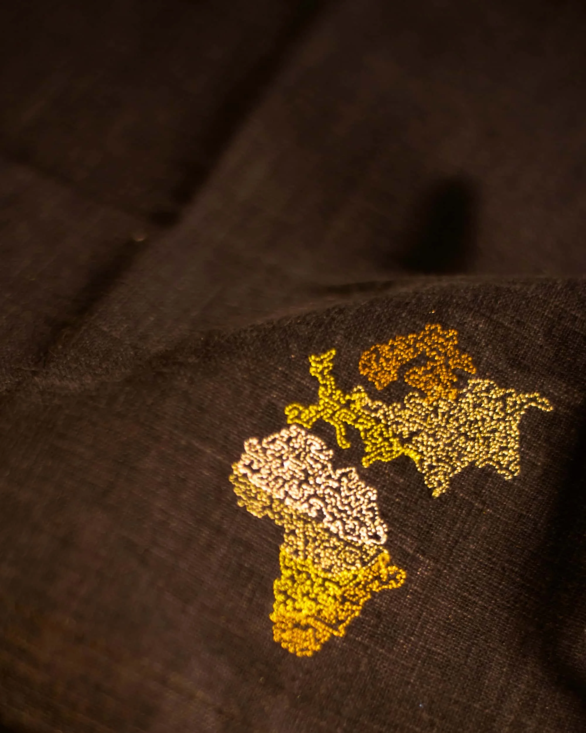Close-up of a fabric with a pattern of small, yellow, interconnected shapes on a black background.