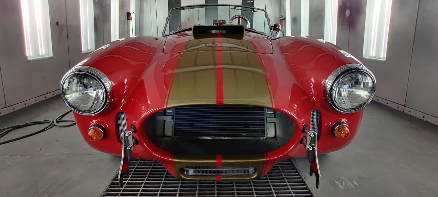 Front view of a classic red race car with gold accents, parked inside a well-lit garage.