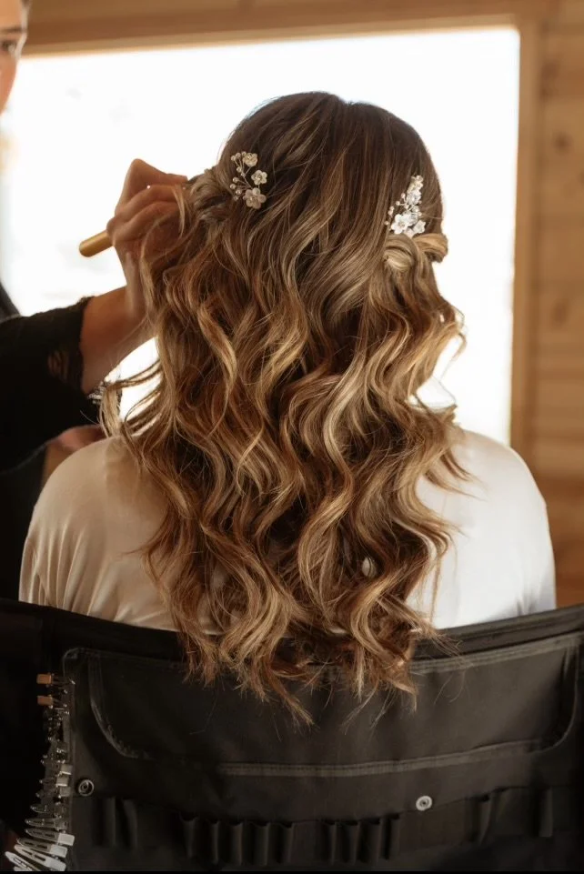 A woman with long, curly hair having her hair styled with floral hair accessories by a stylist.