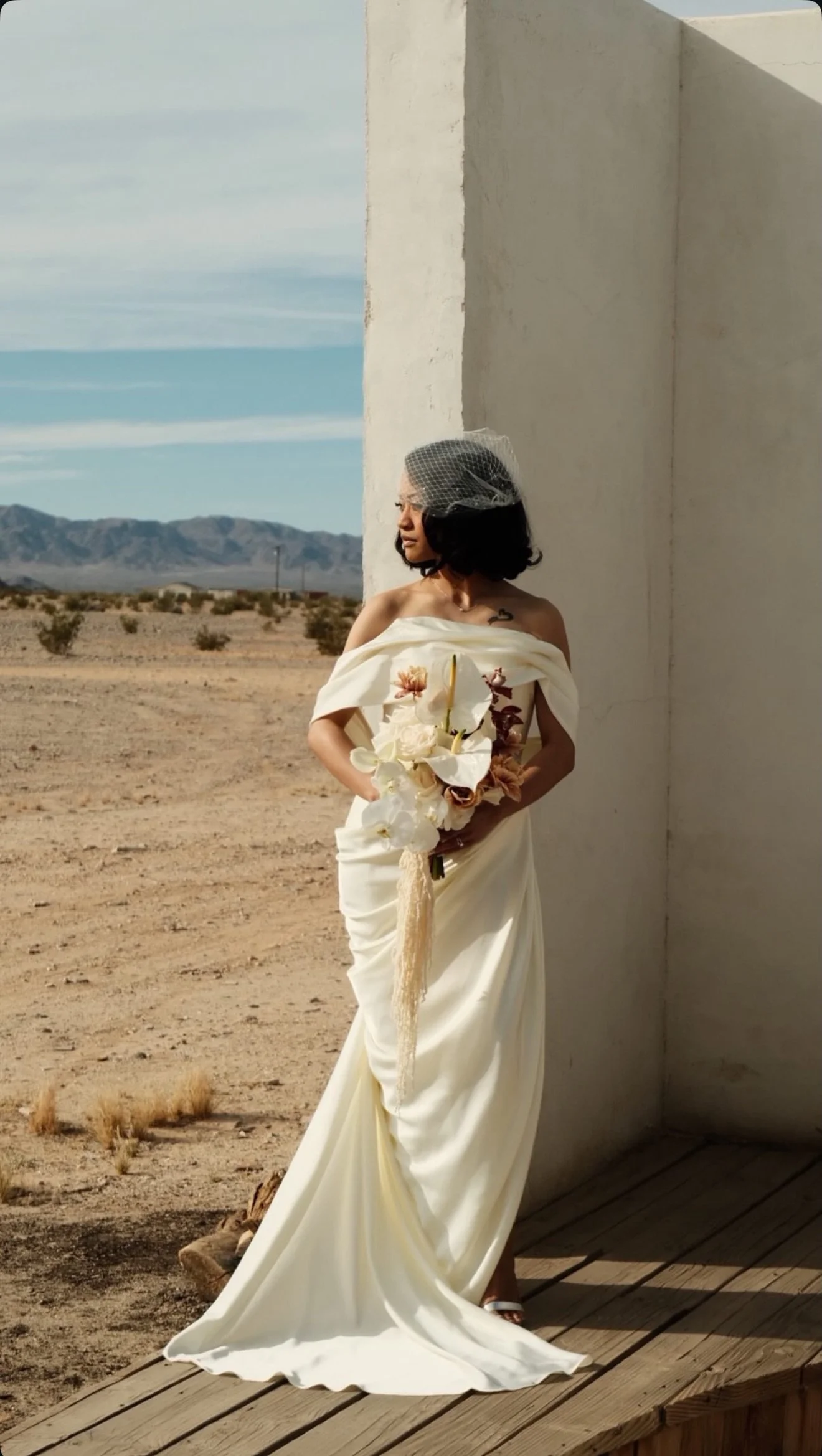 Bride in hair and makeup by Danielle Rose Beauty Atelier gazing out ward into the California landscape. She is grasping her bouquet, and has old Hollywood classic wedding style for her dress, veil, and hair and makeup.
