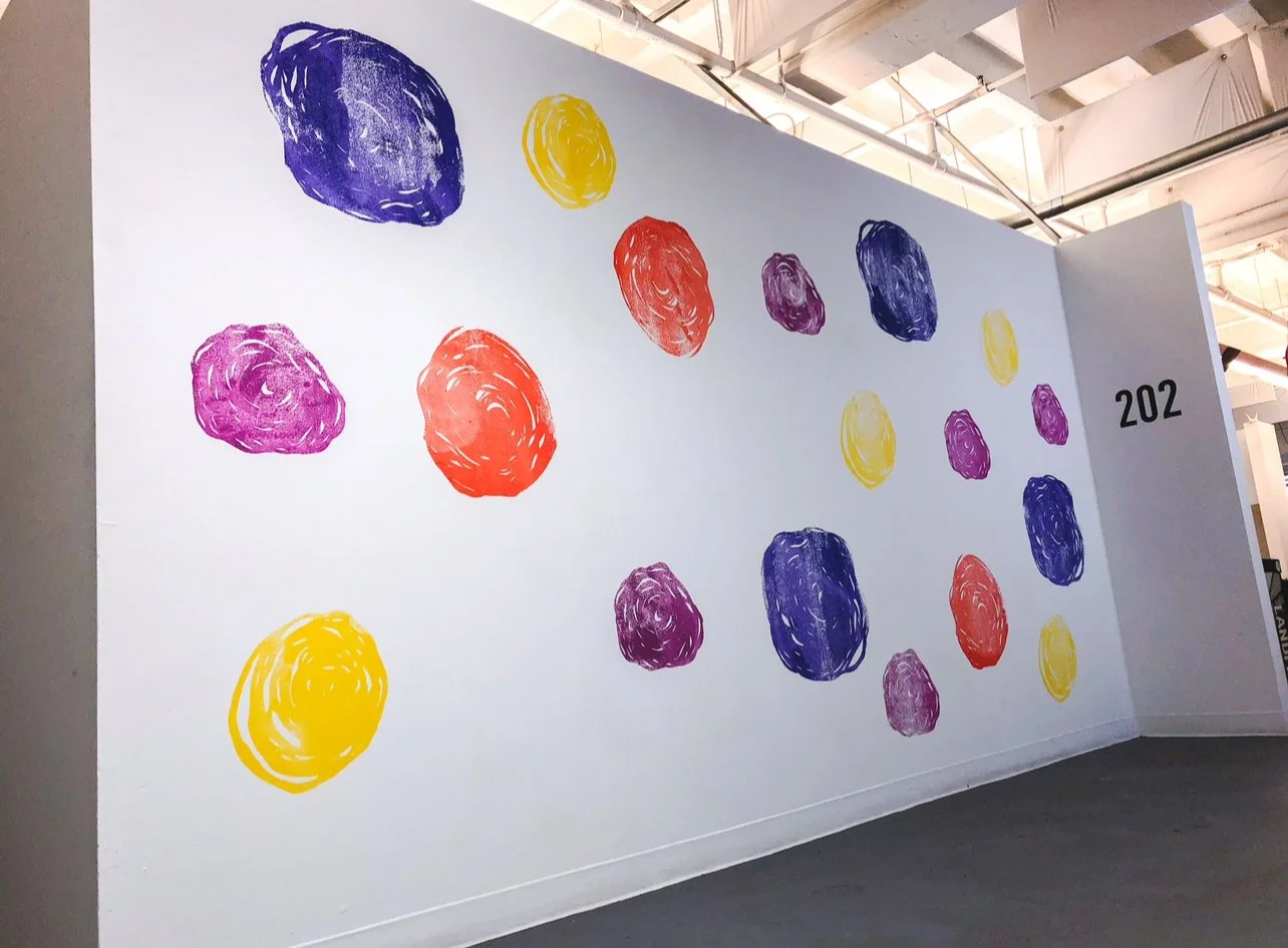 Abstract colorful circles and blobs in yellow, red, purple, and pink on a white gallery wall with the number 202.