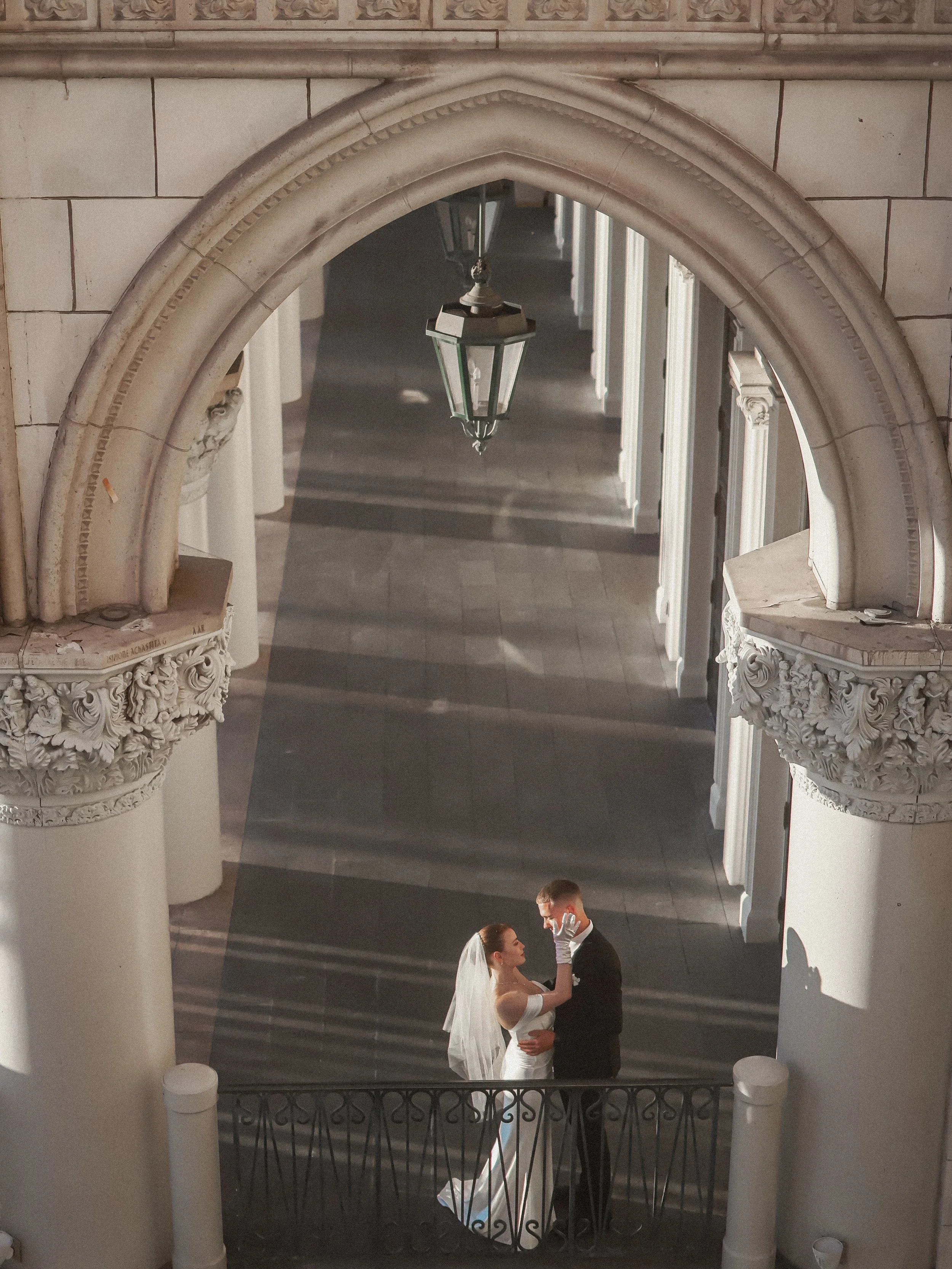 A bride and groom sharing a moment on a staircase inside a historic building with ornate architectural details.