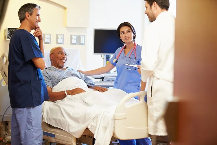Hospital room with a patient in a bed speaking with three healthcare professionals, including two doctors and a nurse.