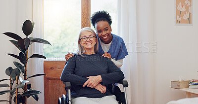 A smiling elderly woman in a wheelchair with a caregiver standing behind her, both looking at the camera in a bright room.