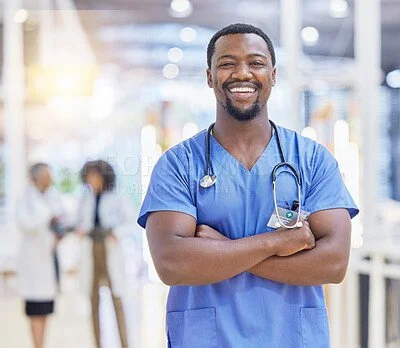 A smiling male nurse in blue scrubs standing with arms crossed in a hospital setting.