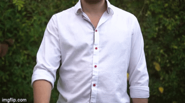 Part of a person wearing a white button-up shirt with red details, standing outdoors with trees in the background.