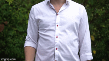 Person wearing a white button-up shirt with rolled-up sleeves standing outdoors with greenery in the background.