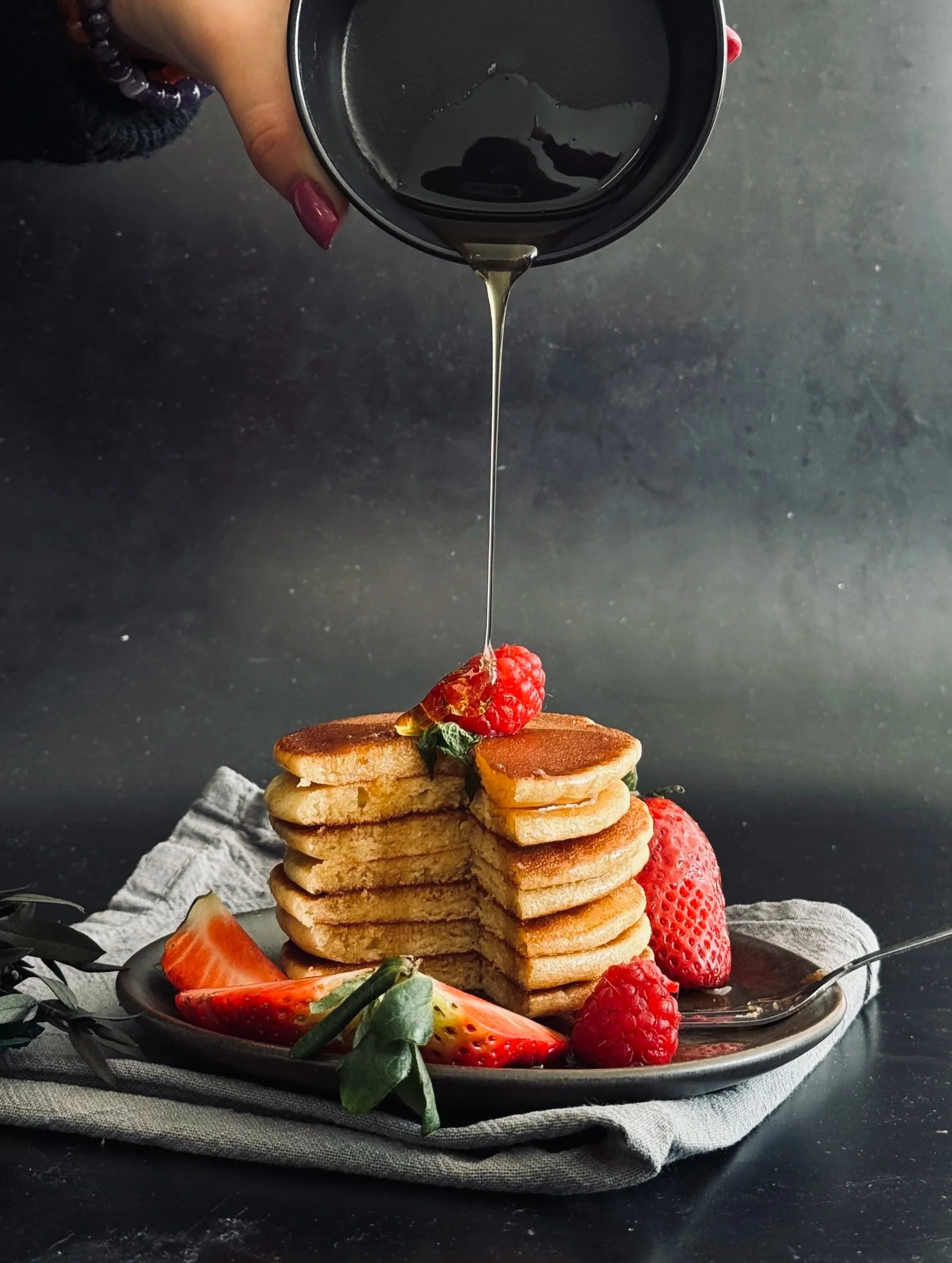 Pancakes empilés avec des fruits rouges, avec du sirop d'érable étant versé dessus.