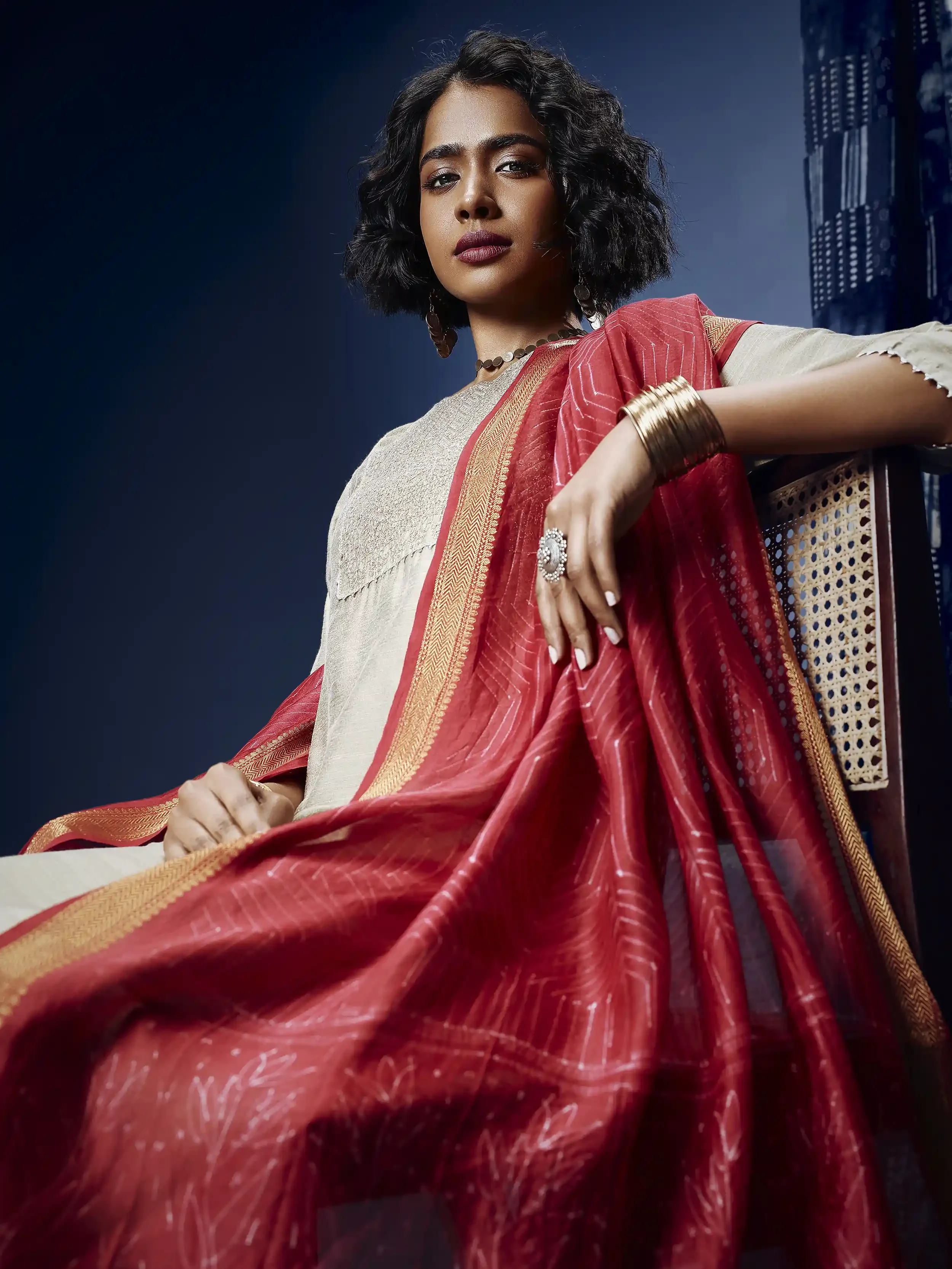 A woman dressed in traditional Indian attire reclining on a chair with a dark background. Anandclix, Bangalore, advertising photographer, Fashion photographer, Editorial photographer, Bangalore photographer.