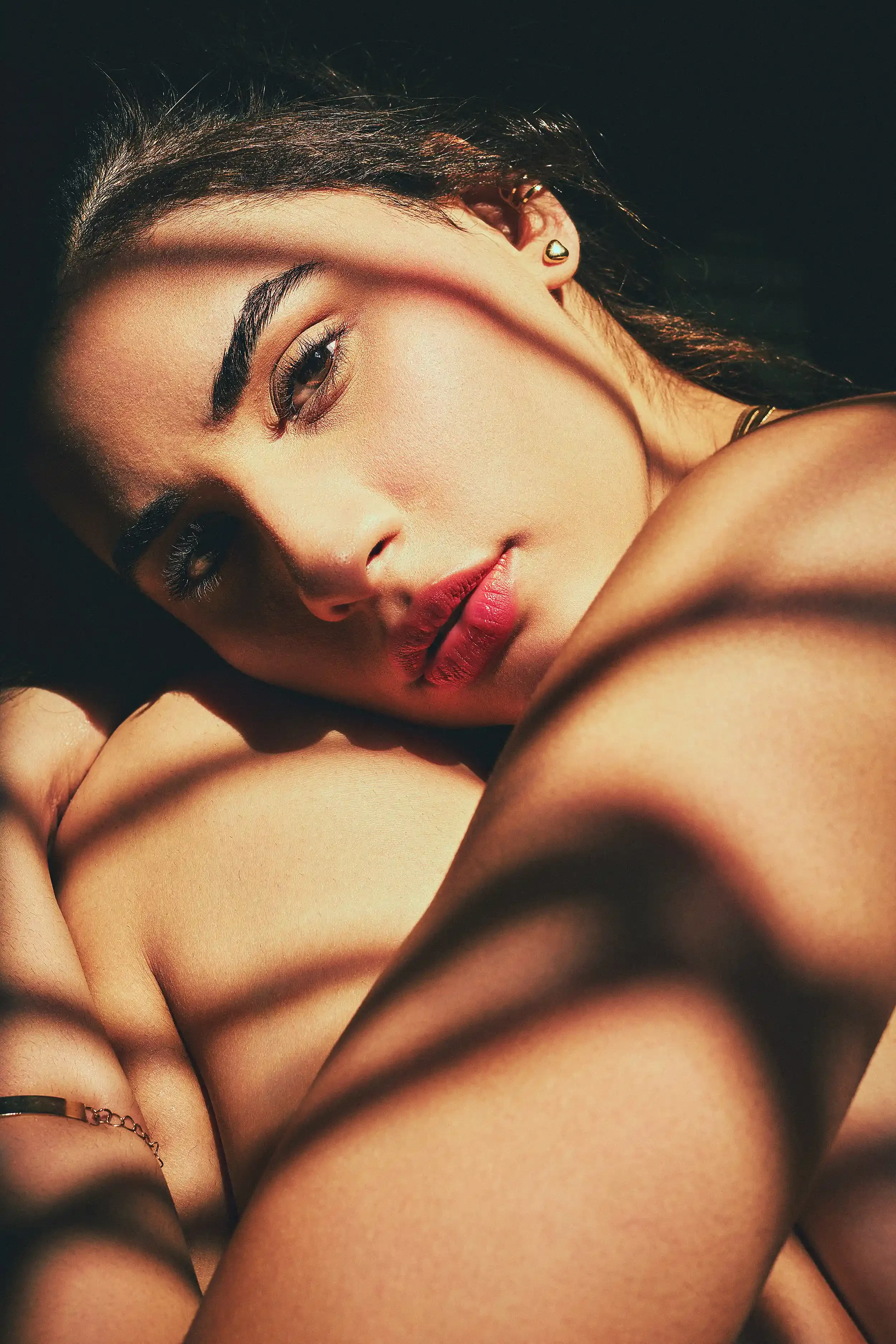 A close-up of a woman with dark hair and makeup resting her head on her shoulder, with shadows cast across her face and body. Anandclix, Bangalore, advertising photographer, Fashion photographer, Editorial photographer, Bangalore photographer.