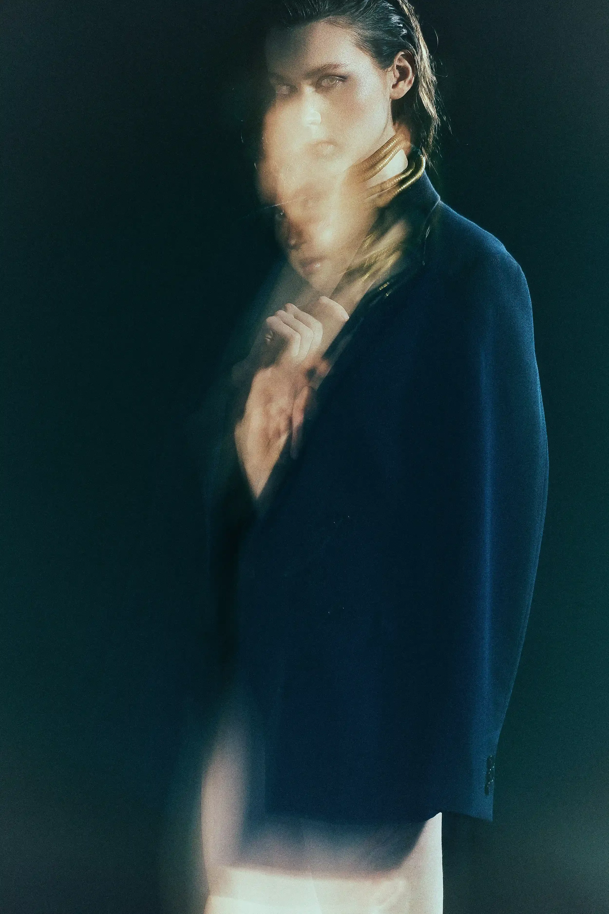 A woman with dark hair, wearing a navy blazer, with a blurred reflection or double exposure effect against a dark background. Anandclix, Bangalore, advertising photographer, Fashion photographer, Editorial photographer, Bangalore photographer.