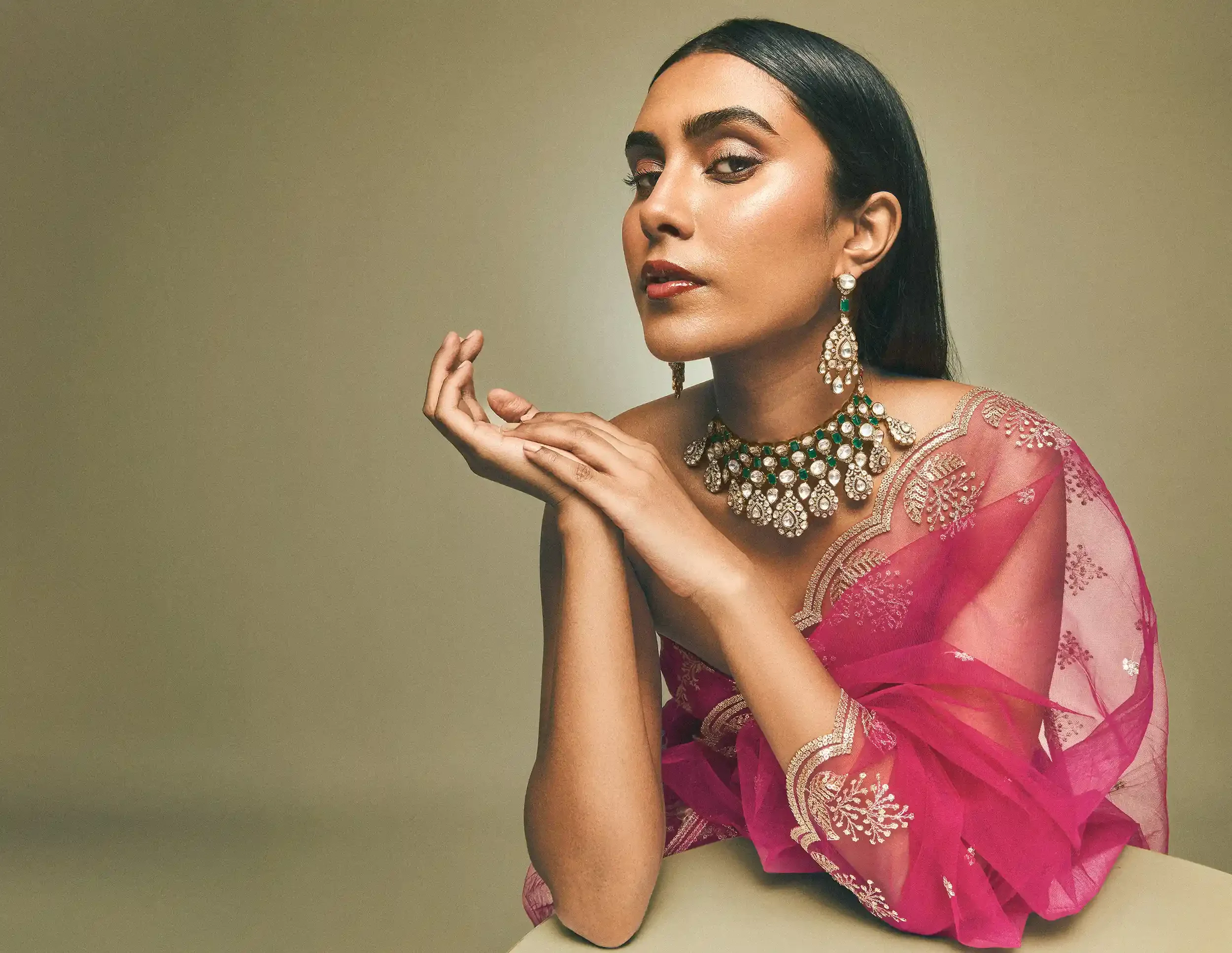 A woman with dark hair and fair skin, wearing a blue dress and jewellery, including earrings, a necklace, and a ring, rests her chin on her hand and smiles gently. Kushal's Fashion Jewellery, Anandclix, Bangalore, advertising photographer, Fashion.